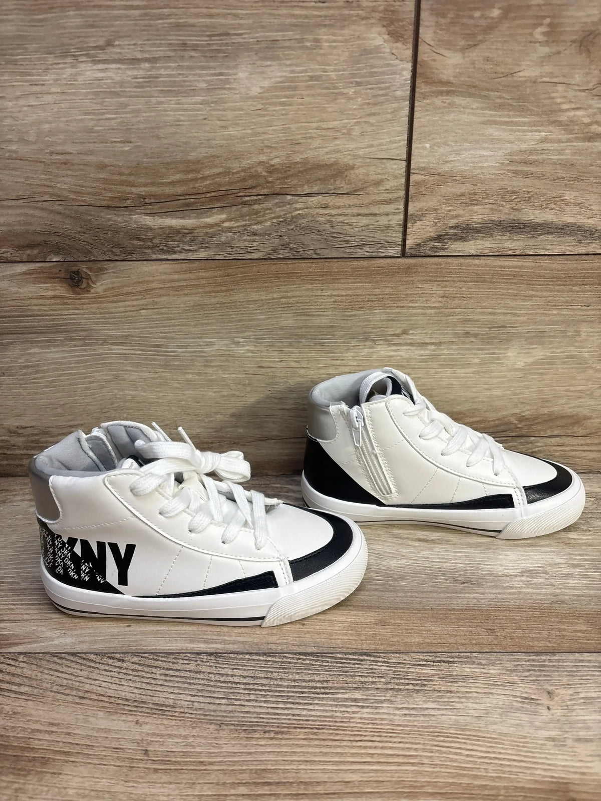 Side view of white DKNY Hannah Leena high-top girls sneakers with black trim, side zipper, laces, and DKNY logo on wood floor