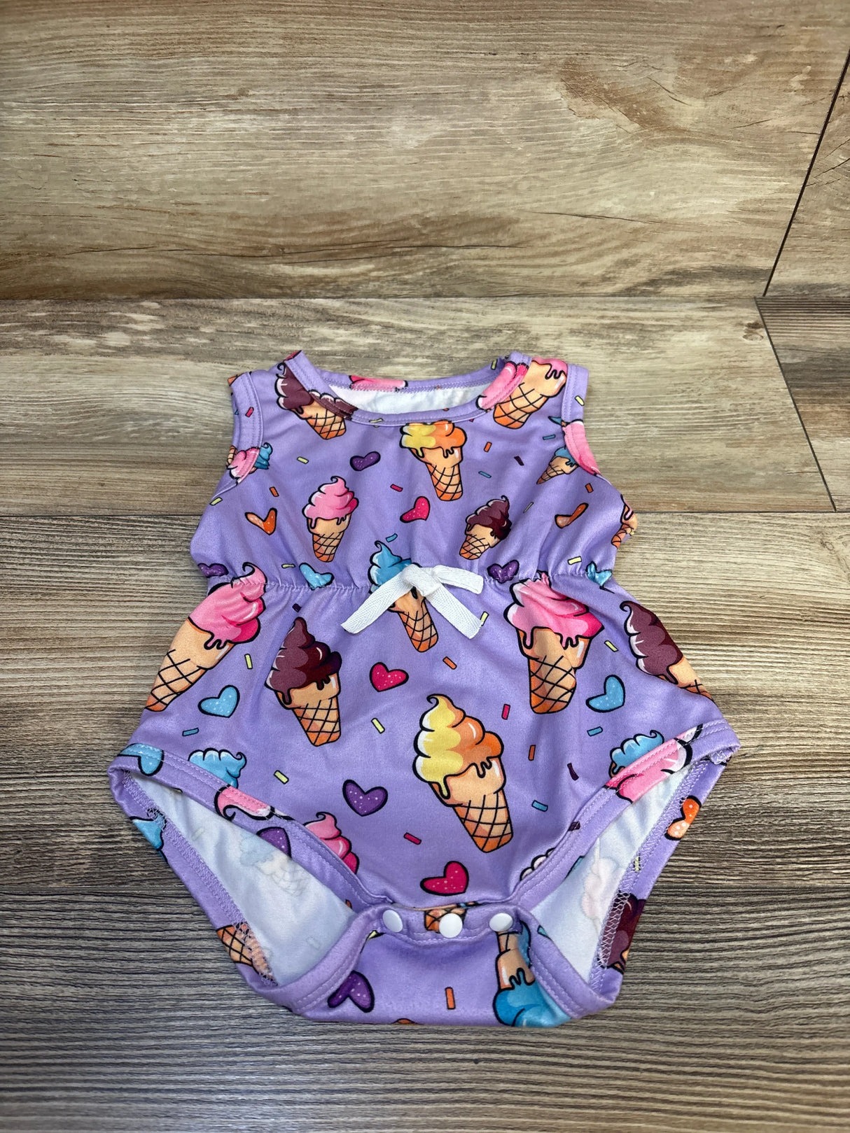 Front view of purple tank bodysuit with ice cream and heart print, white bow and snap crotch on wood background