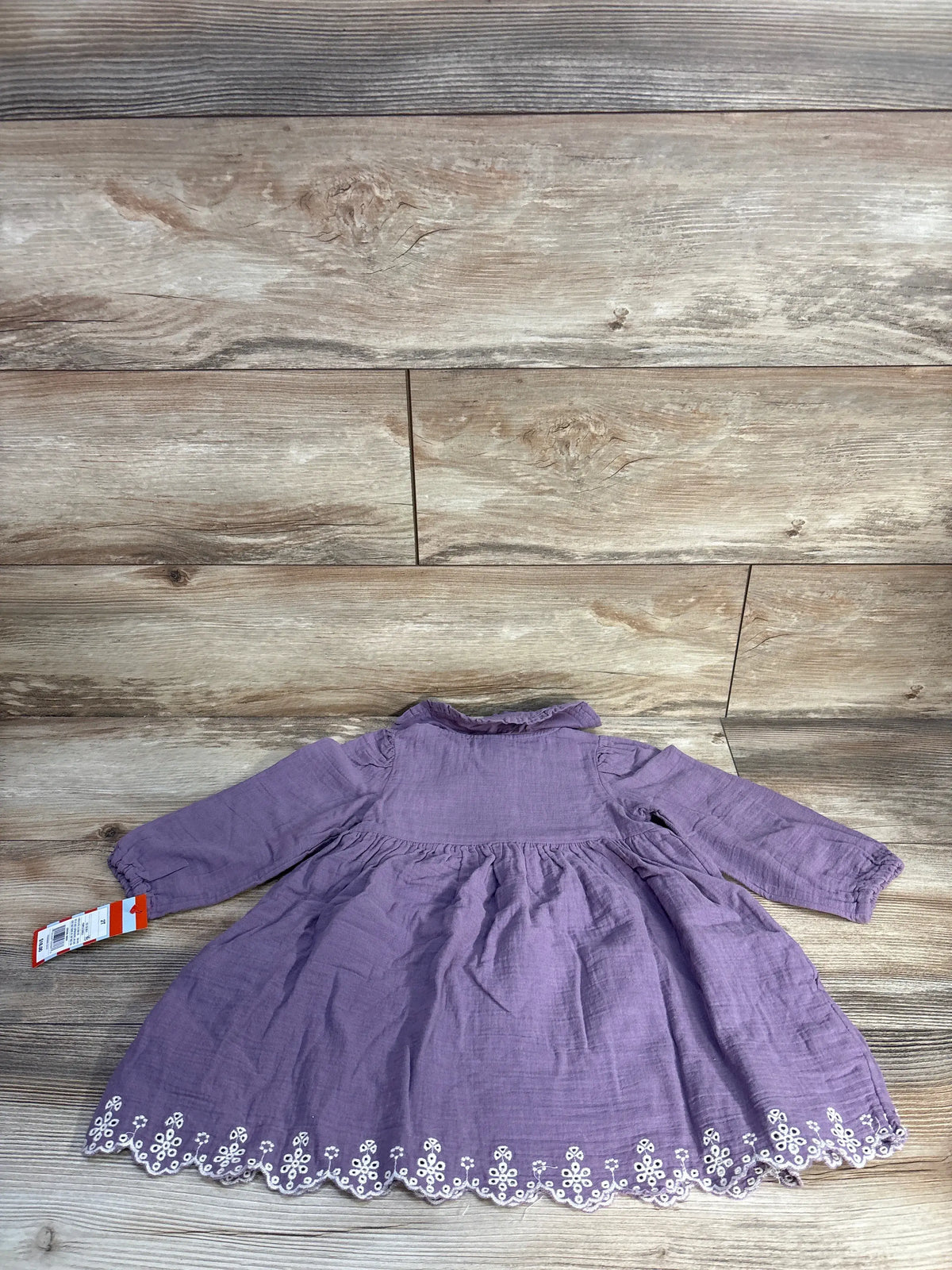 Back flat lay of mauve Cat & Jack gauze toddler dress showing eyelet scalloped hem and attached tag on wood background