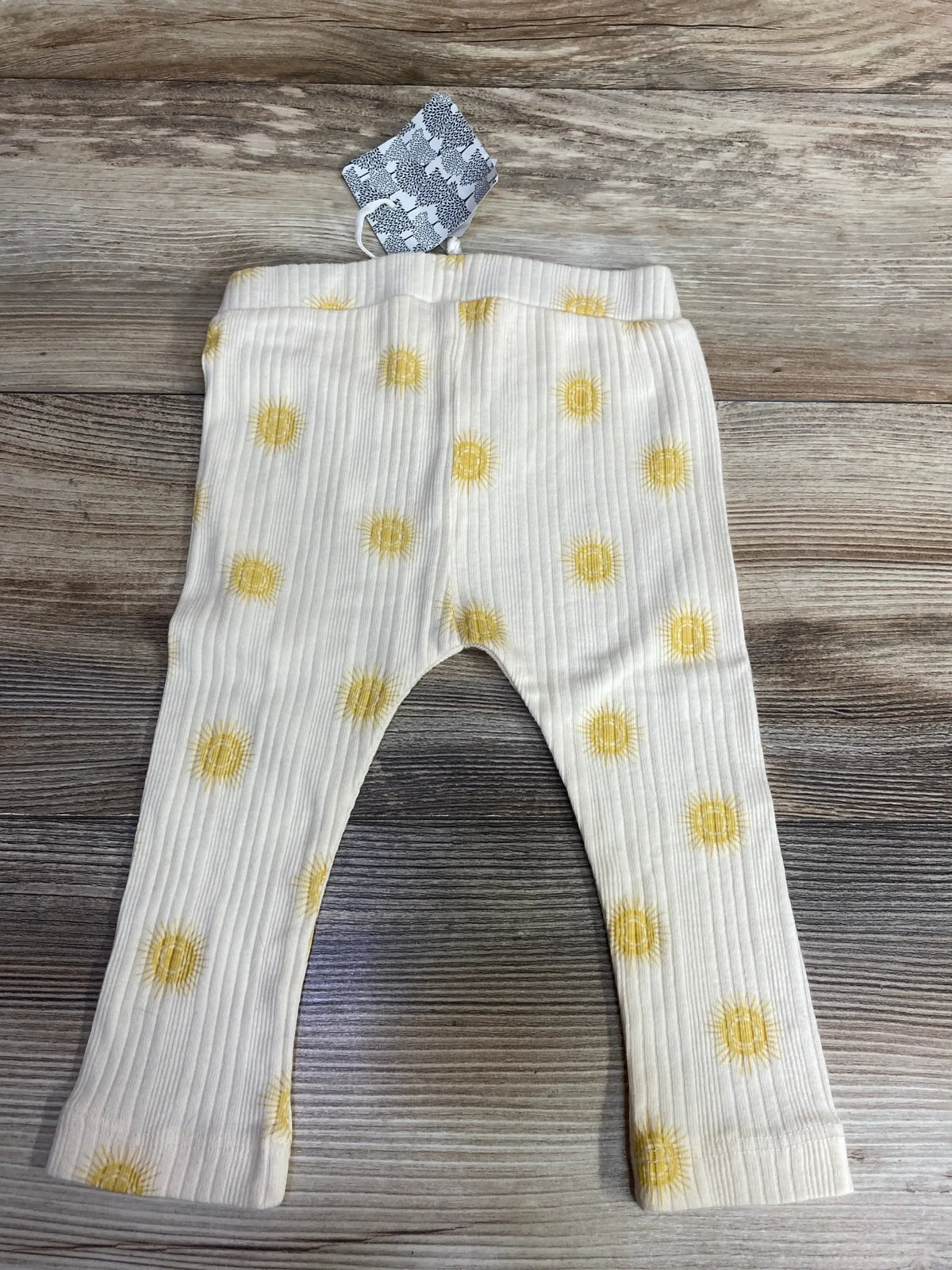 White ribbed baby leggings with yellow sun print pattern on wooden surface