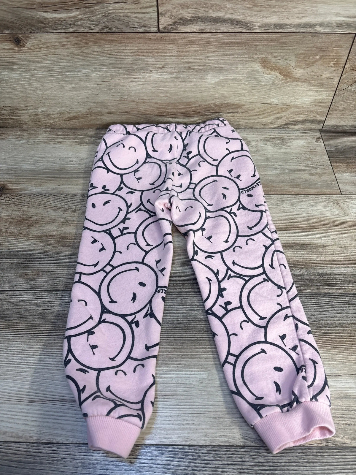 Pink kids jogger pants with black smiley face print on wood background
