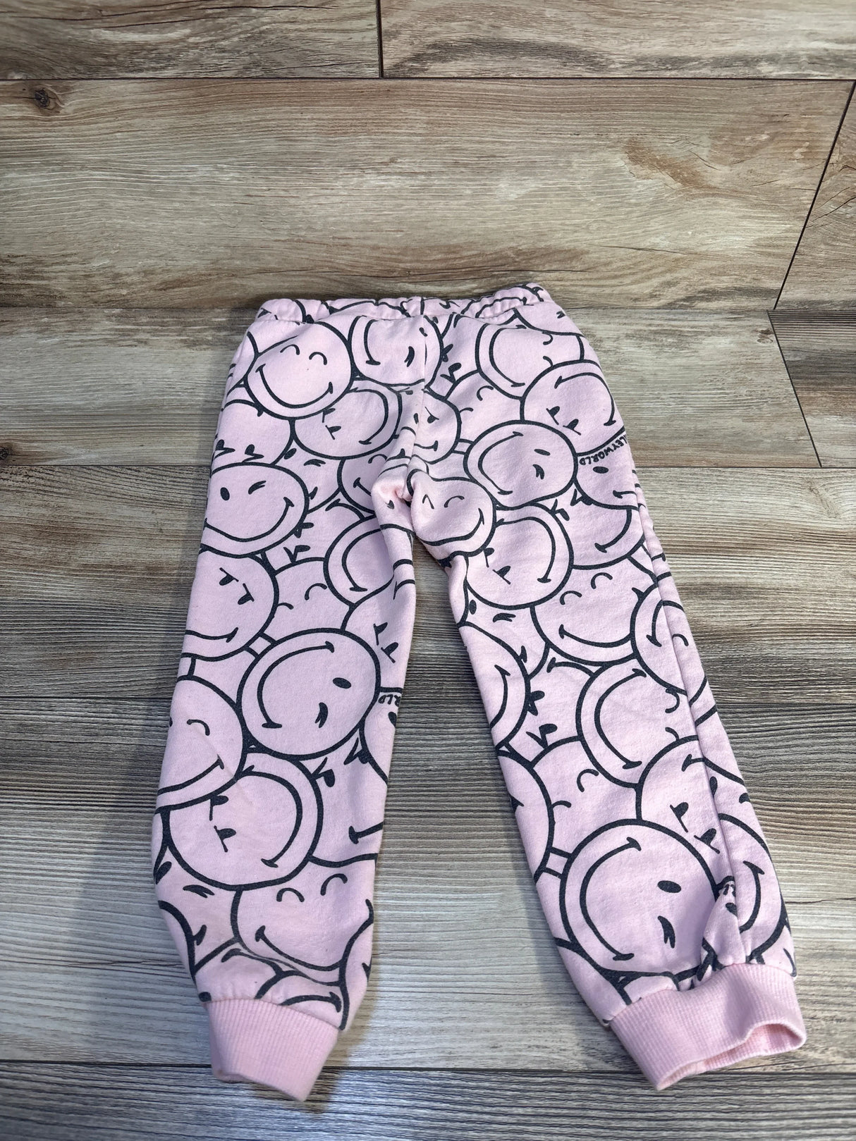Pink kids jogger pants with black smiley face print on wood background