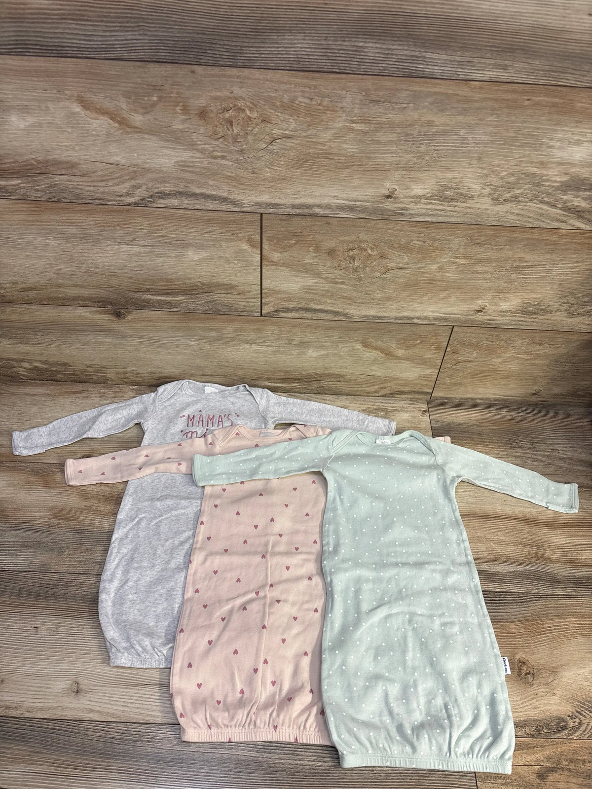 Top-down view of three Gerber baby sleep gowns in mint, with long sleeves and gathered open bottoms on a wood floor