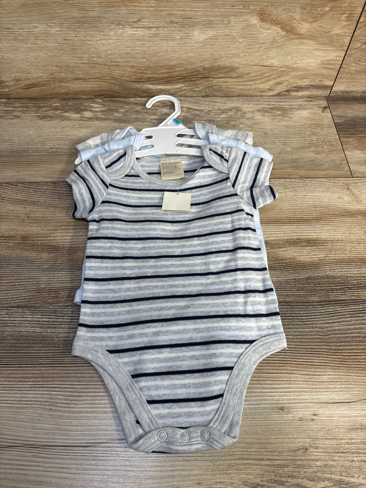 Top view of a grey striped baby bodysuit from a 3-pack showing short sleeves and three snap closures on wood background