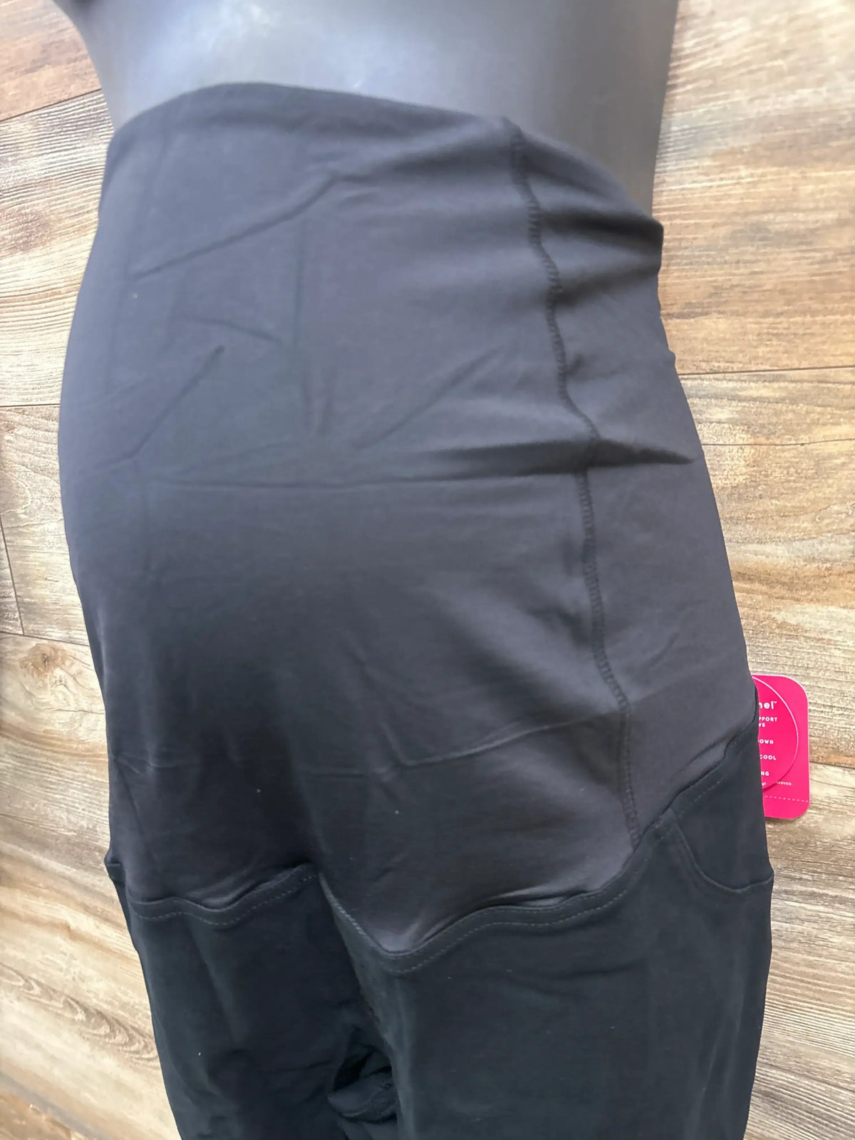 Side view of black maternity utility jeggings with high over-belly panel and cargo pocket on mannequin with wood background