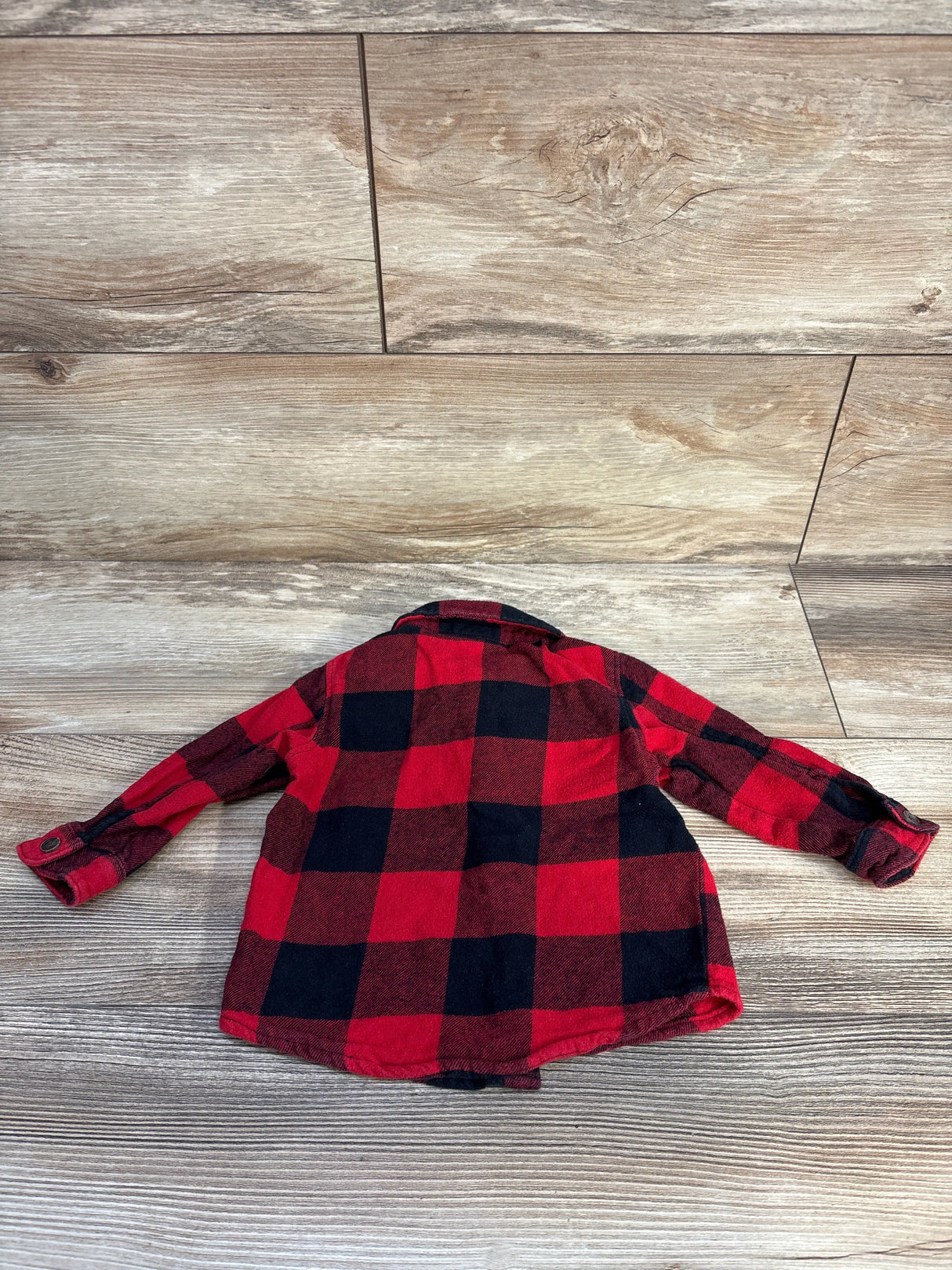 Red and black plaid flannel shirt on wood floor, back view, casual kids clothing