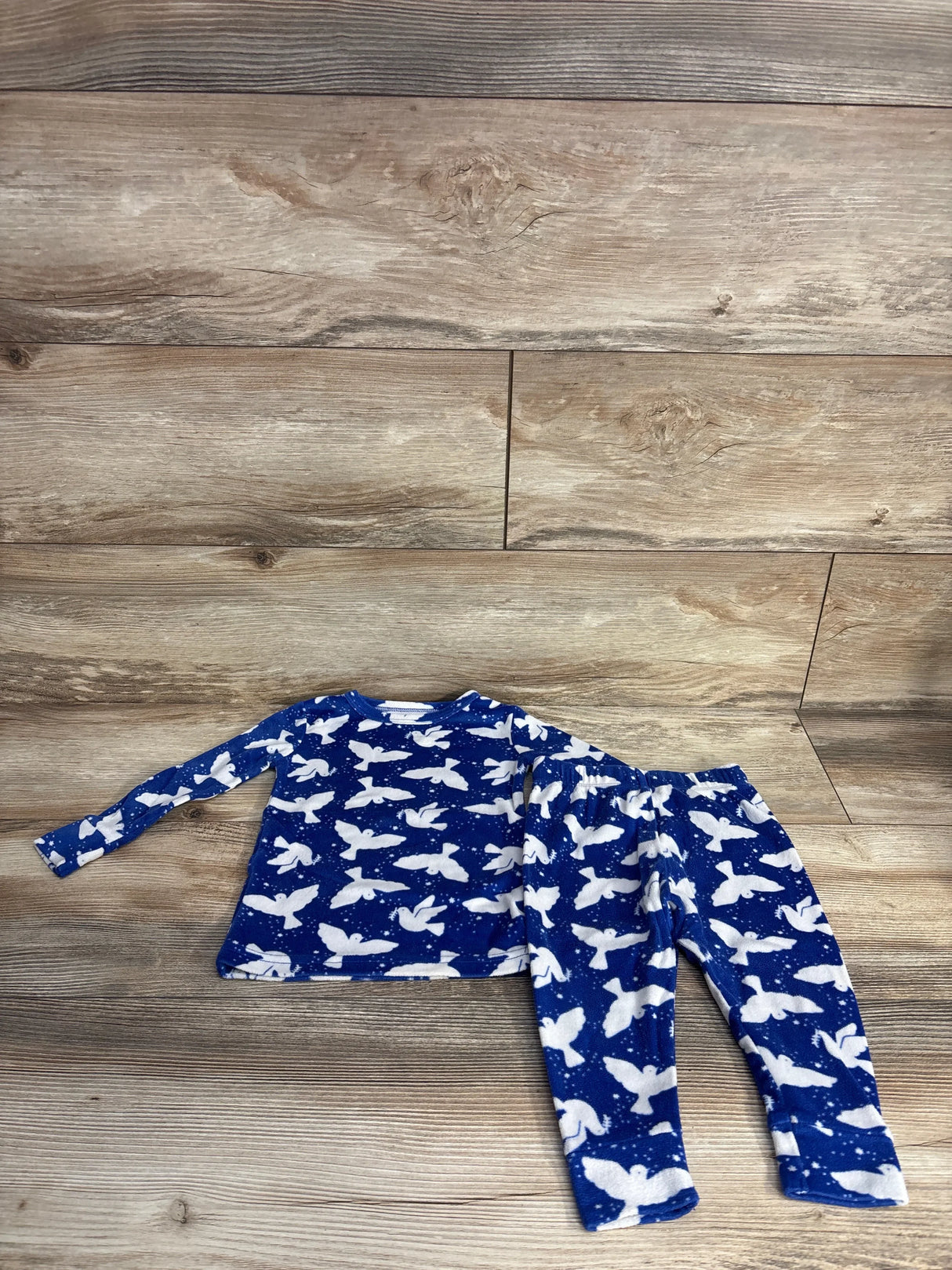 Blue children's pajama set with white bird pattern laid on wooden floor