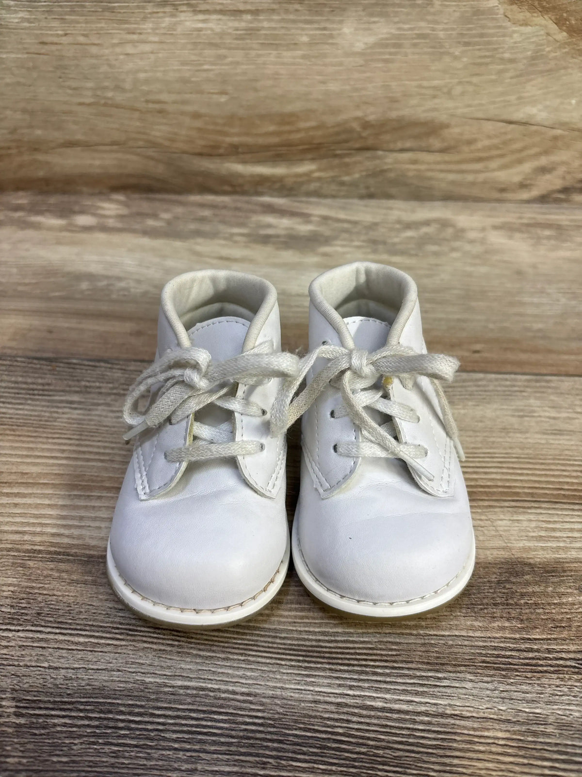 Front view of Teeny Toes First Walker baby shoes in white showing lace-up closure and padded collar on wood background