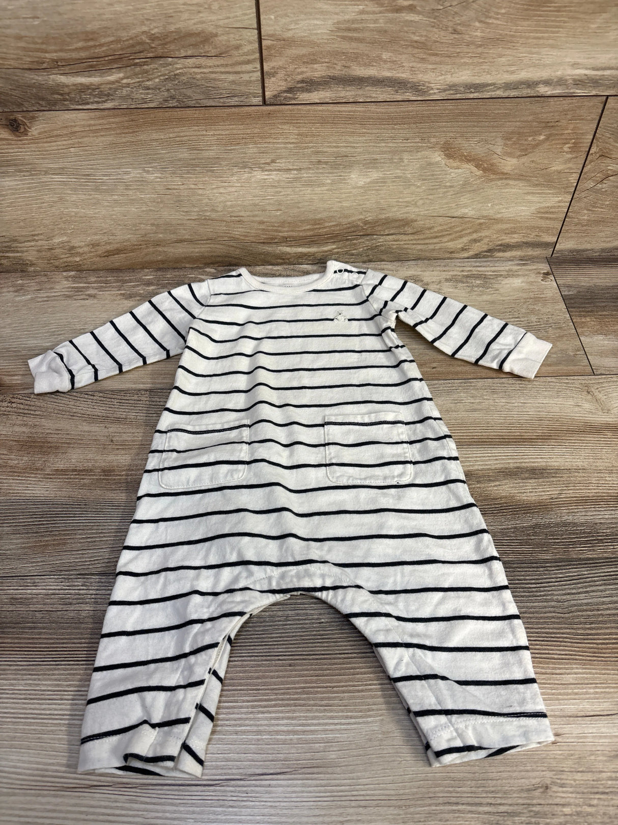 White baby romper with black horizontal stripes and pockets on wood floor