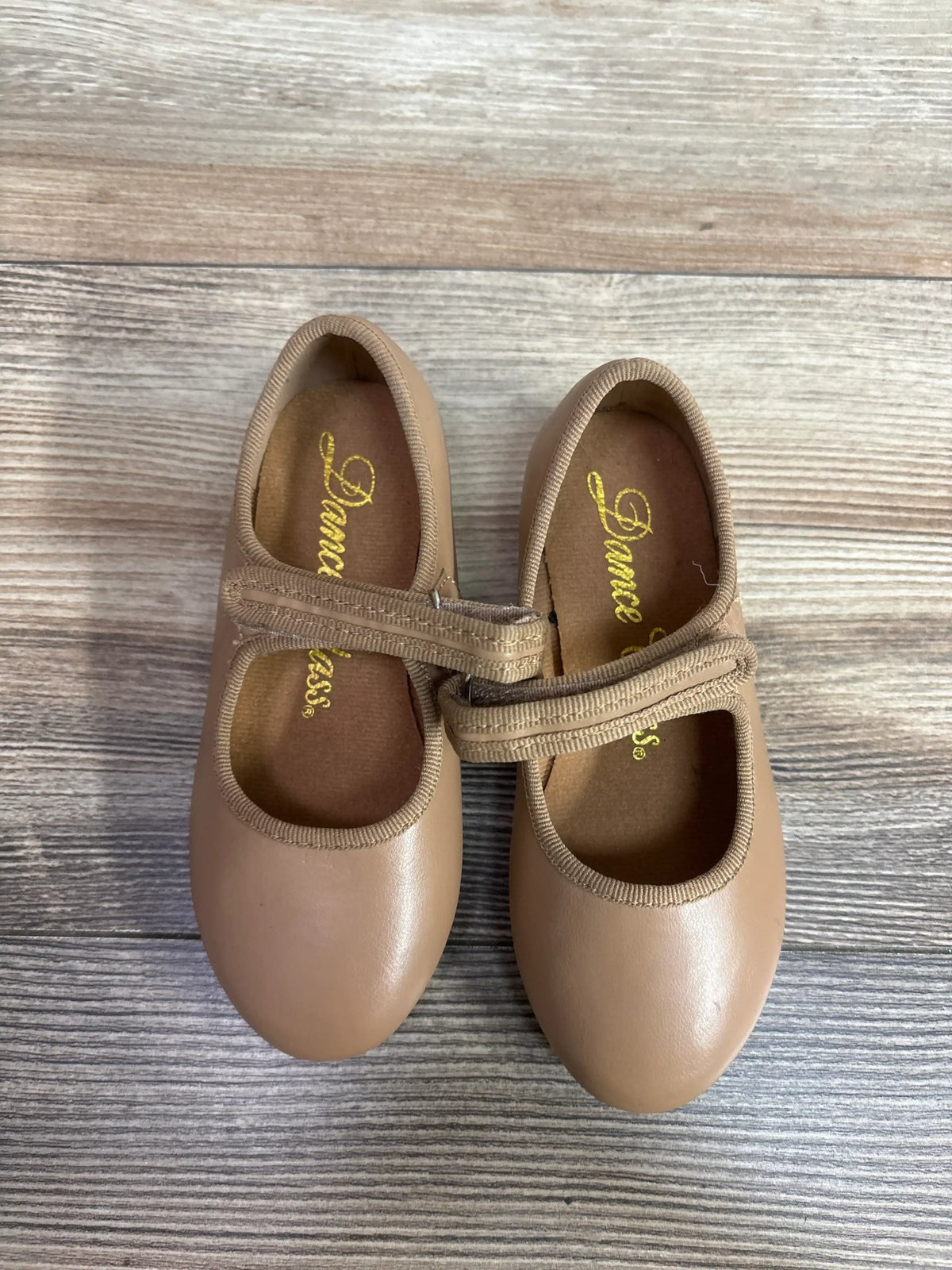Top view of tan tap shoes size 9C with elastic Mary Jane straps and gold Dance Class insole on wood floor