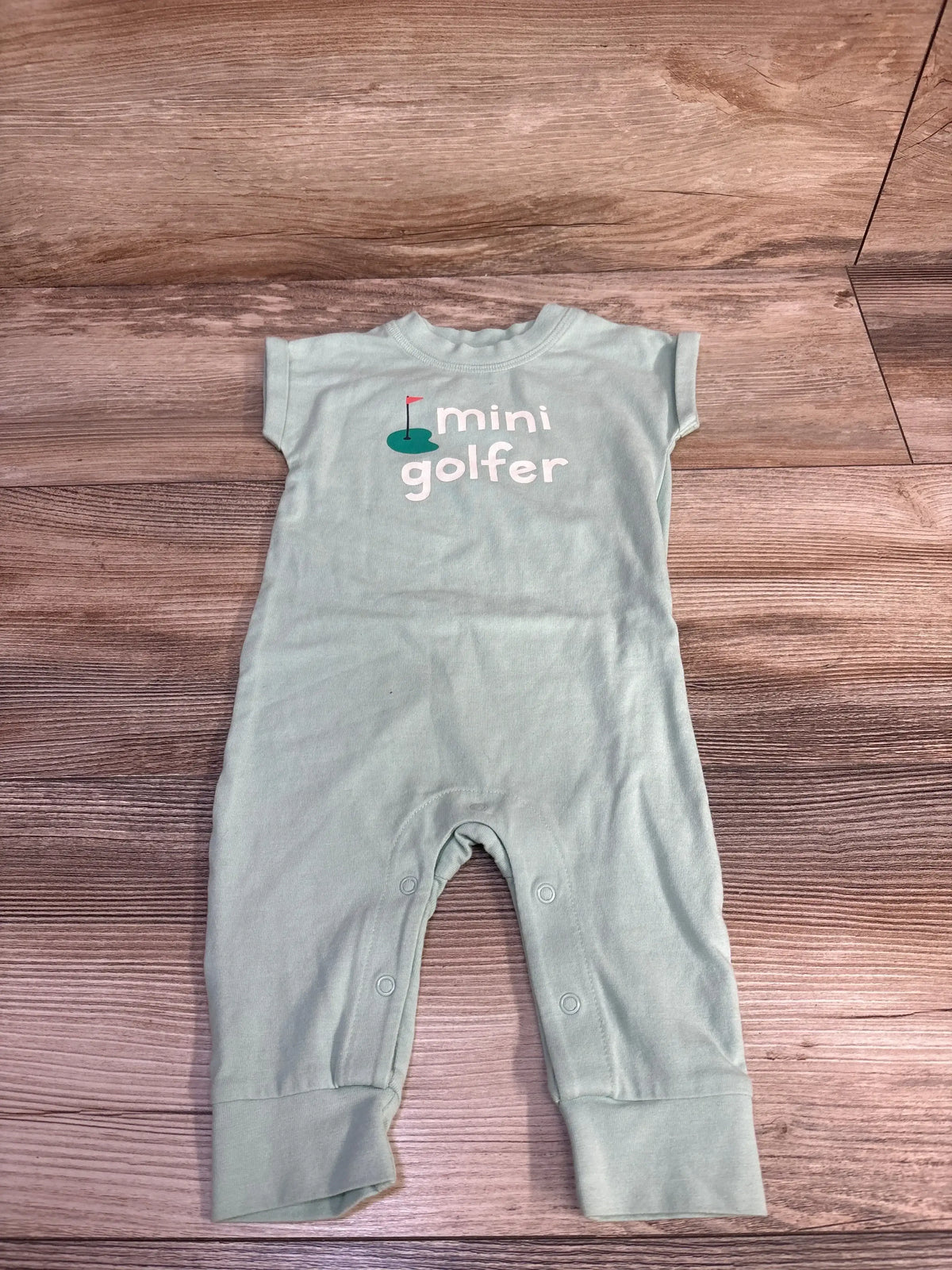 Flat-lay of green Cat & Jack newborn romper showing mini golfer chest print and snap leg closures on wood background