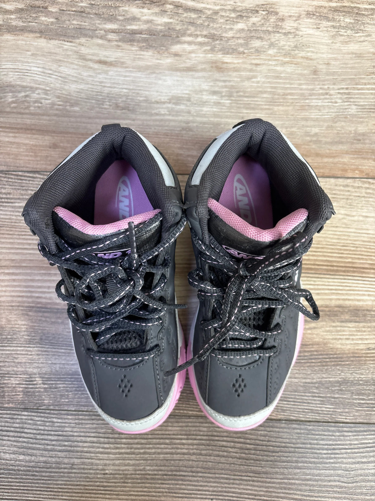 Pair of black and pink children's athletic sneakers with laces on wooden floor