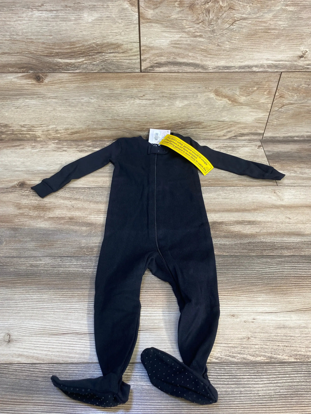 Black footed baby sleeper with zipper, long sleeves and non-slip feet on wood floor