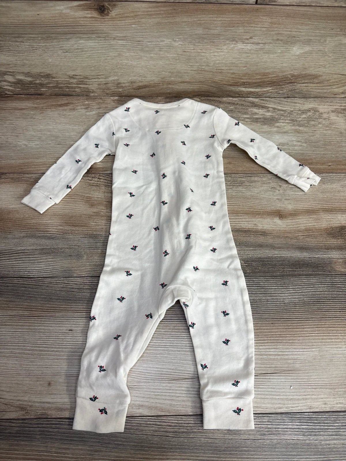 White baby onesie with holly print, long sleeves, laid on wood floor — perfect for holiday baby outfits.