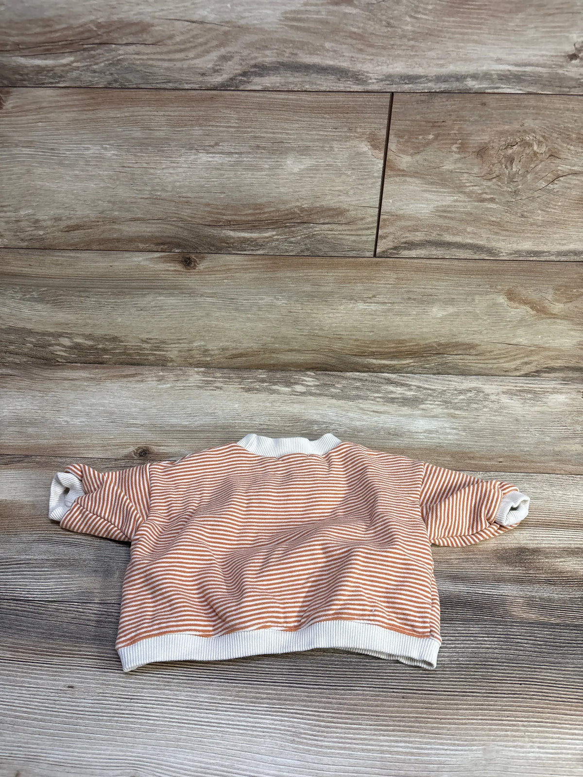 Back view of Roda J baby pullover sweatshirt with orange and white stripes, white ribbed cuffs and hem on wood background
