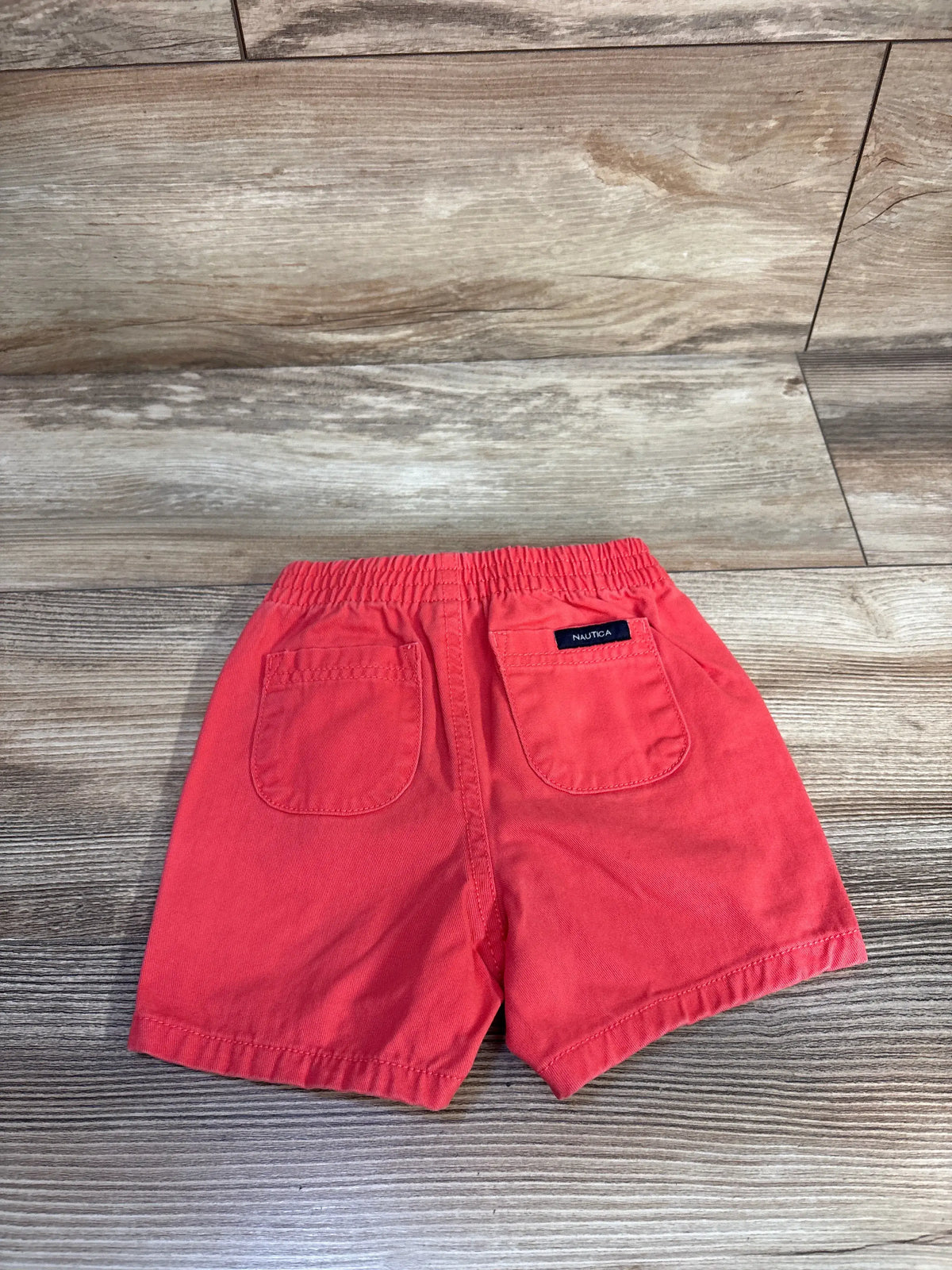 Back view of red Nautica toddler shorts, size 12 months, showcasing drawstring waist and two back pockets on wood-look flooring