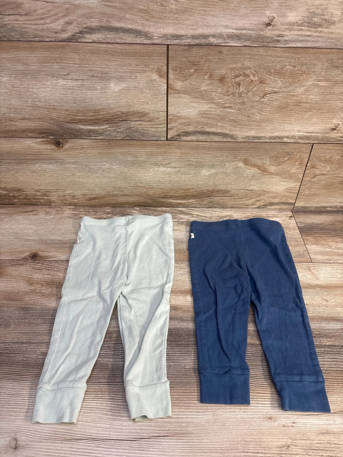 Front view of Burt’s Bees Baby 2pk pull-on pants in blue, size 12 months, showing two pairs with cuffed hems on wood-look flooring