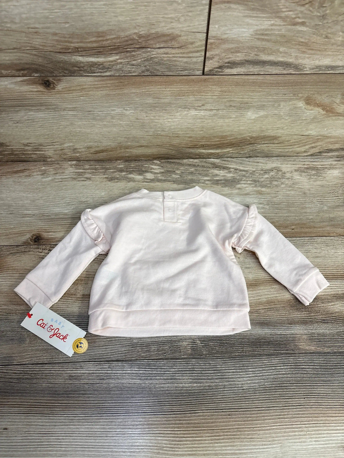 Light pink baby sweater with ruffle sleeves by Cat & Jack on wood background