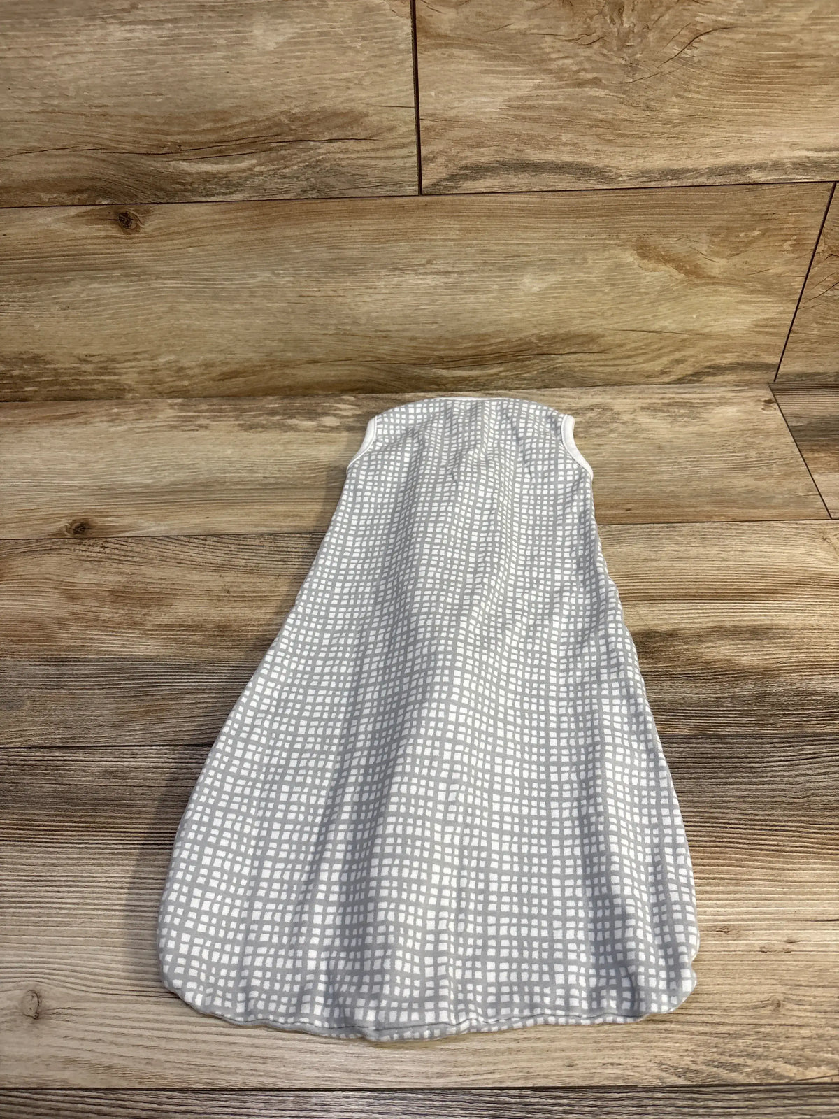 Flat lay of SwaddleMe Night Sack showing grey square-grid print and sleeveless swaddle shape on wood background