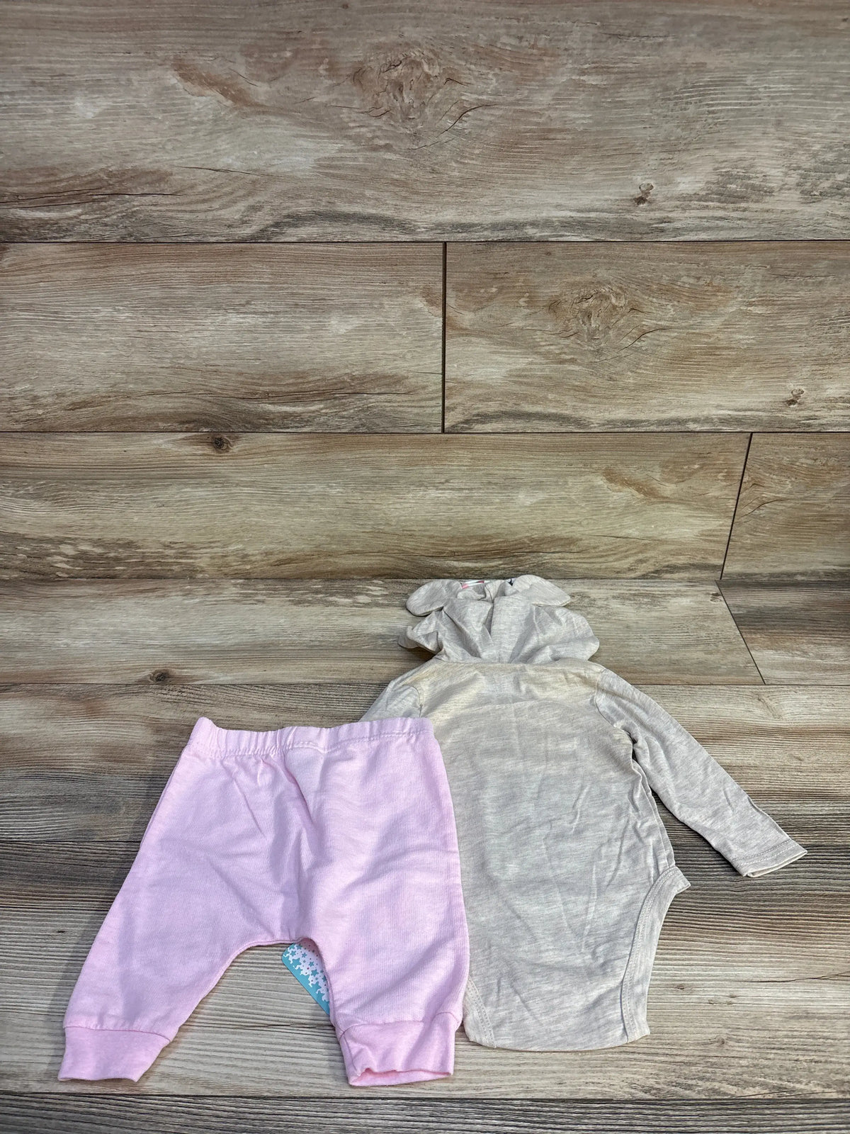 Top-down view of Disney Baby Minnie Mouse two-piece set showcasing gray hooded long-sleeve bodysuit and pink pants on a wood floor