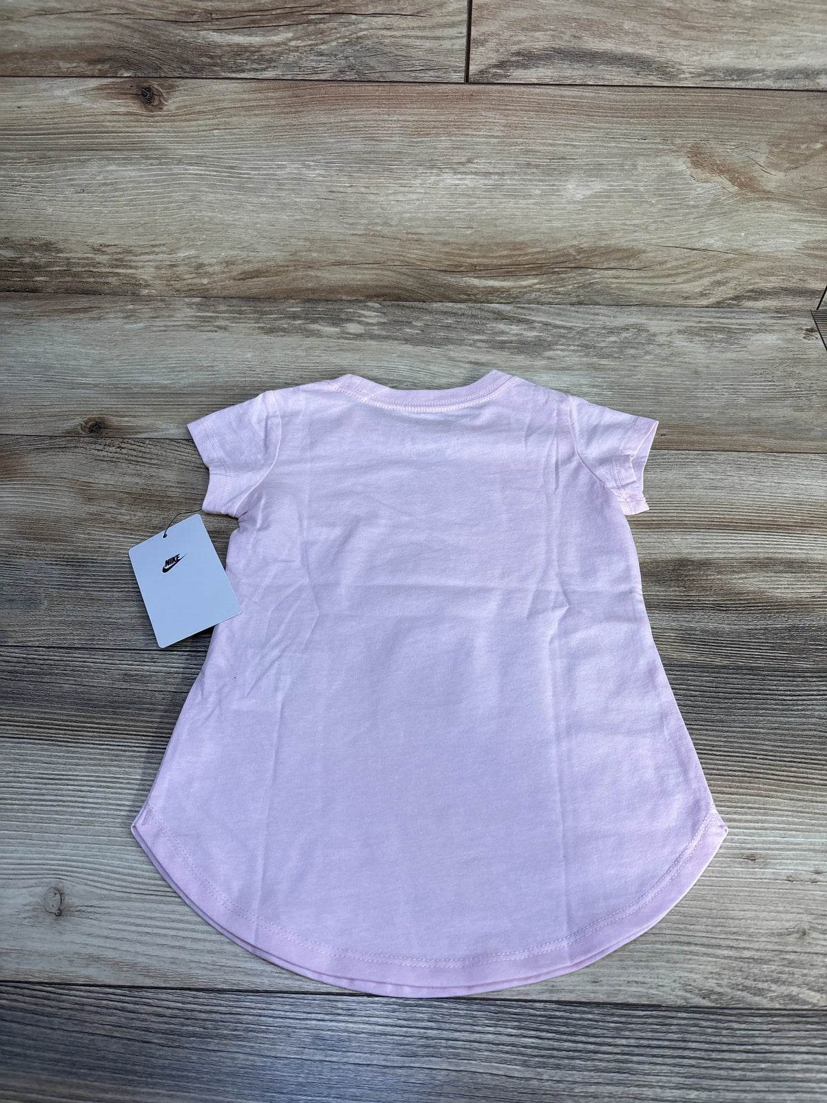 Flat lay of NEW Nike pink foam t-shirt showcasing crew neck, short sleeves, and curved hem on wood grain background