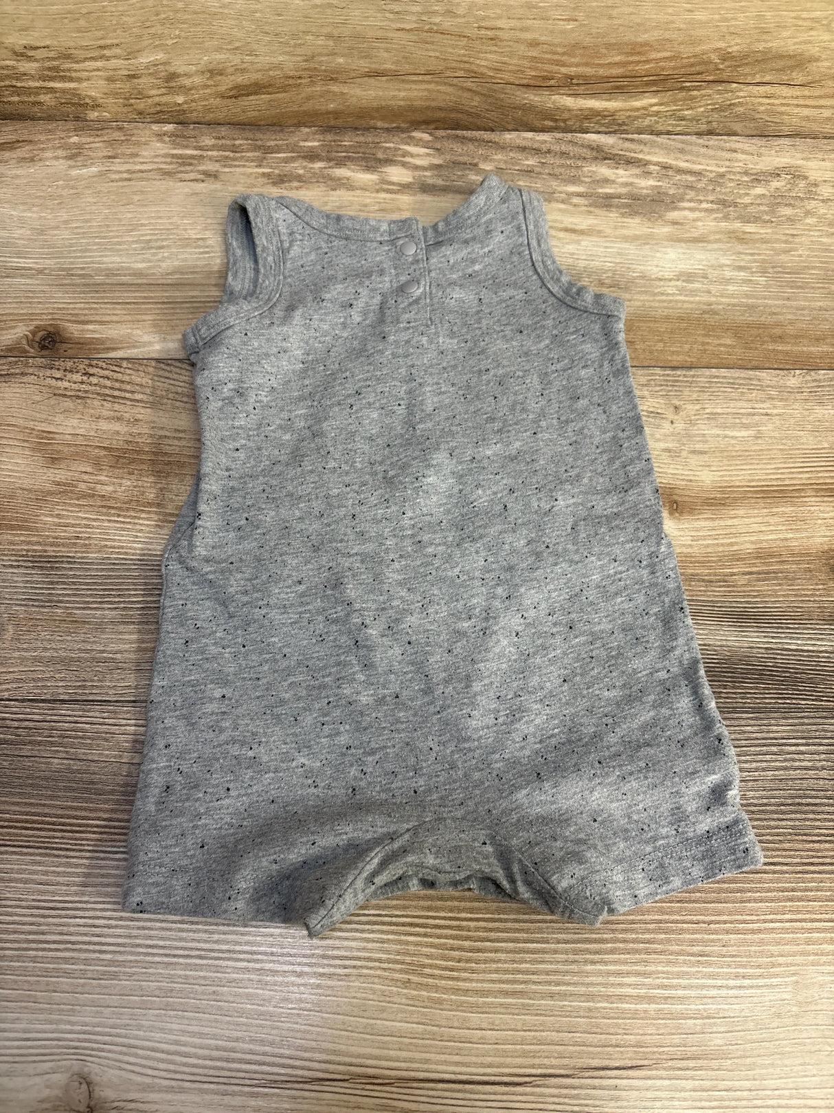 Top down view of grey Nike baby tank shortie romper with sleeveless cut, back snap closures, laid flat on wood background