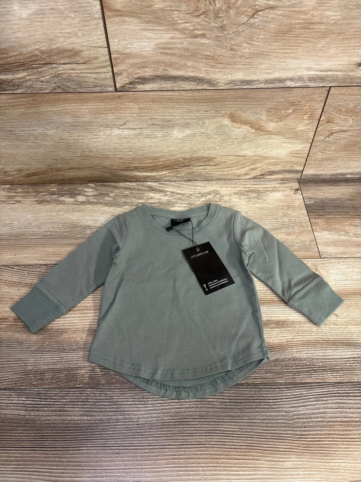 Front view of Little Bipsy newborn long-sleeve tee in olive green with cuffed sleeves and black tag, laid flat on wood floor