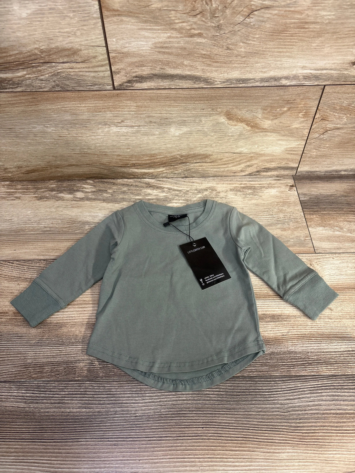 Front view of Little Bipsy newborn long-sleeve tee in olive green with cuffed sleeves and black tag, laid flat on wood floor