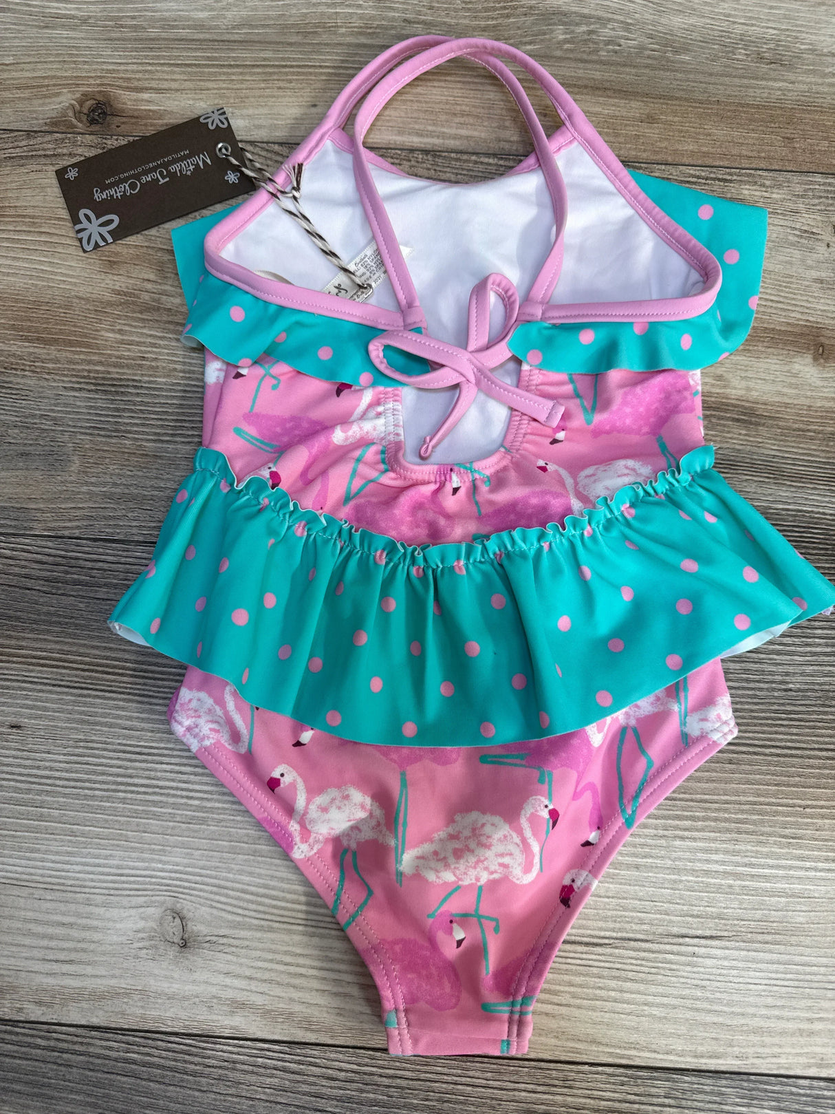 Pink and teal toddler girl swimsuit with flamingo print and polka dot ruffle, flat lay