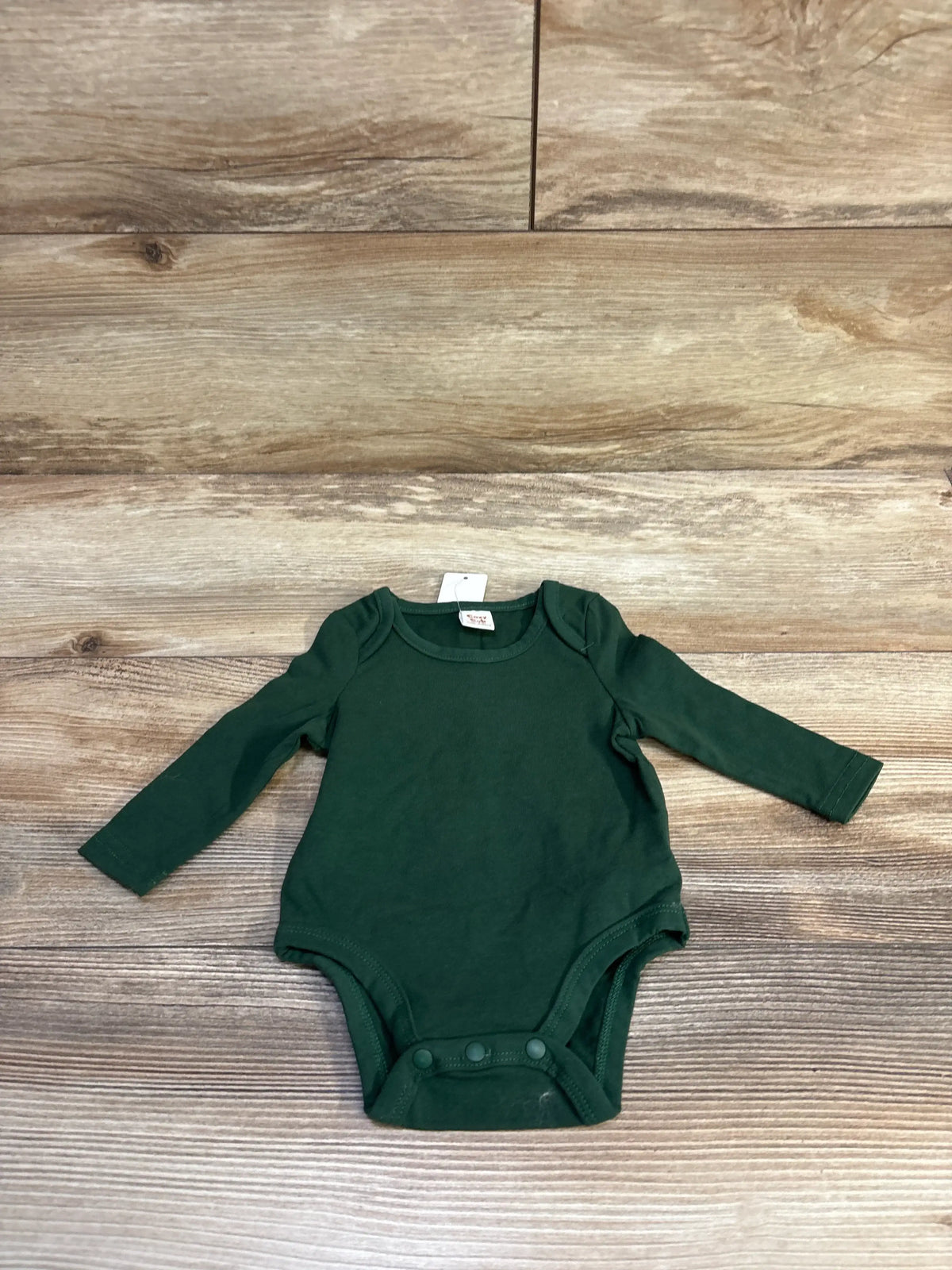 New Cozy Cub long sleeve baby bodysuit in dark green, size 0-1 month, on a wood background