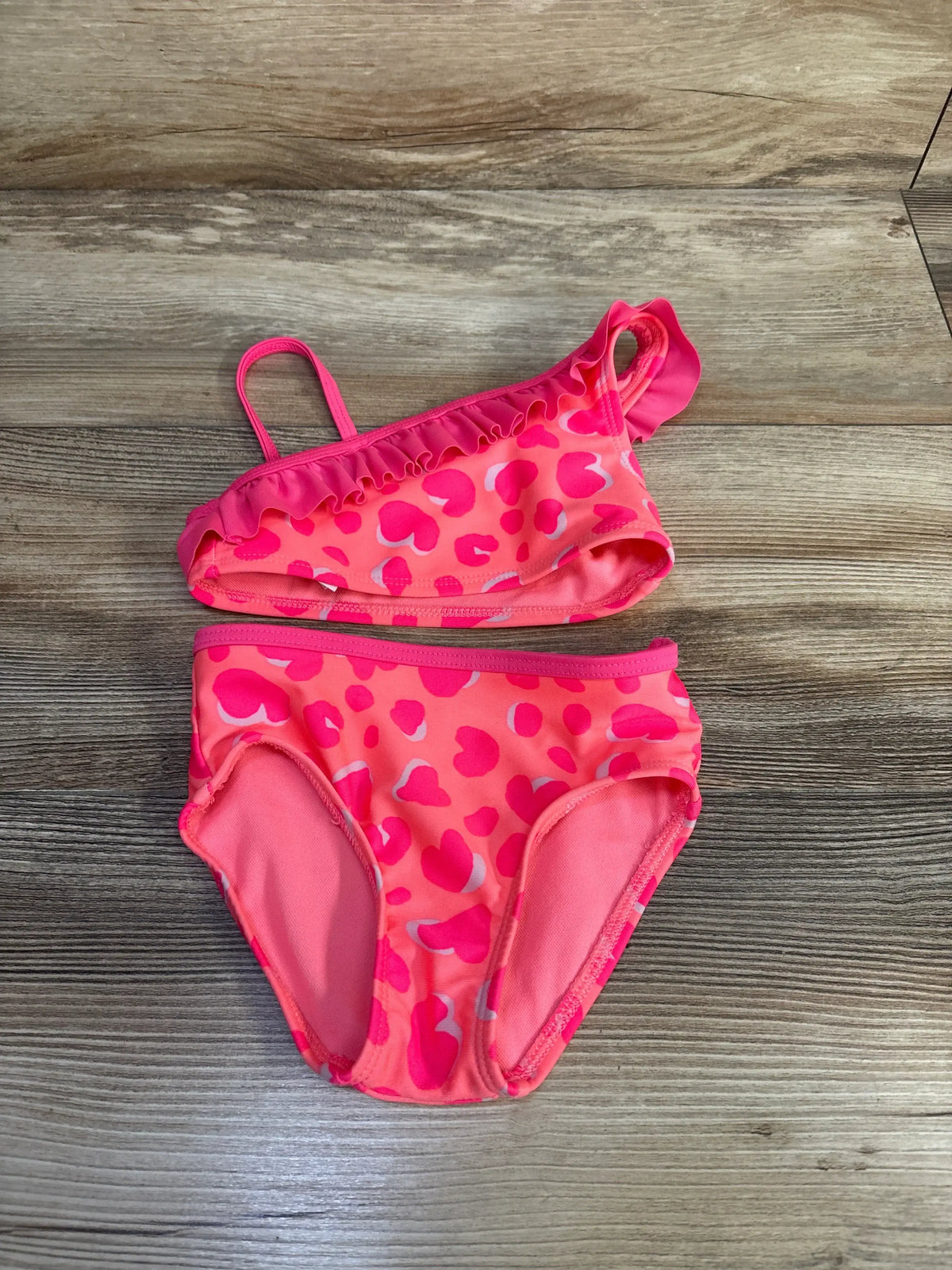 Top-down view of the Cat & Jack two-piece swimsuit showcasing a pink patterned design and ruffled top on a wood surface