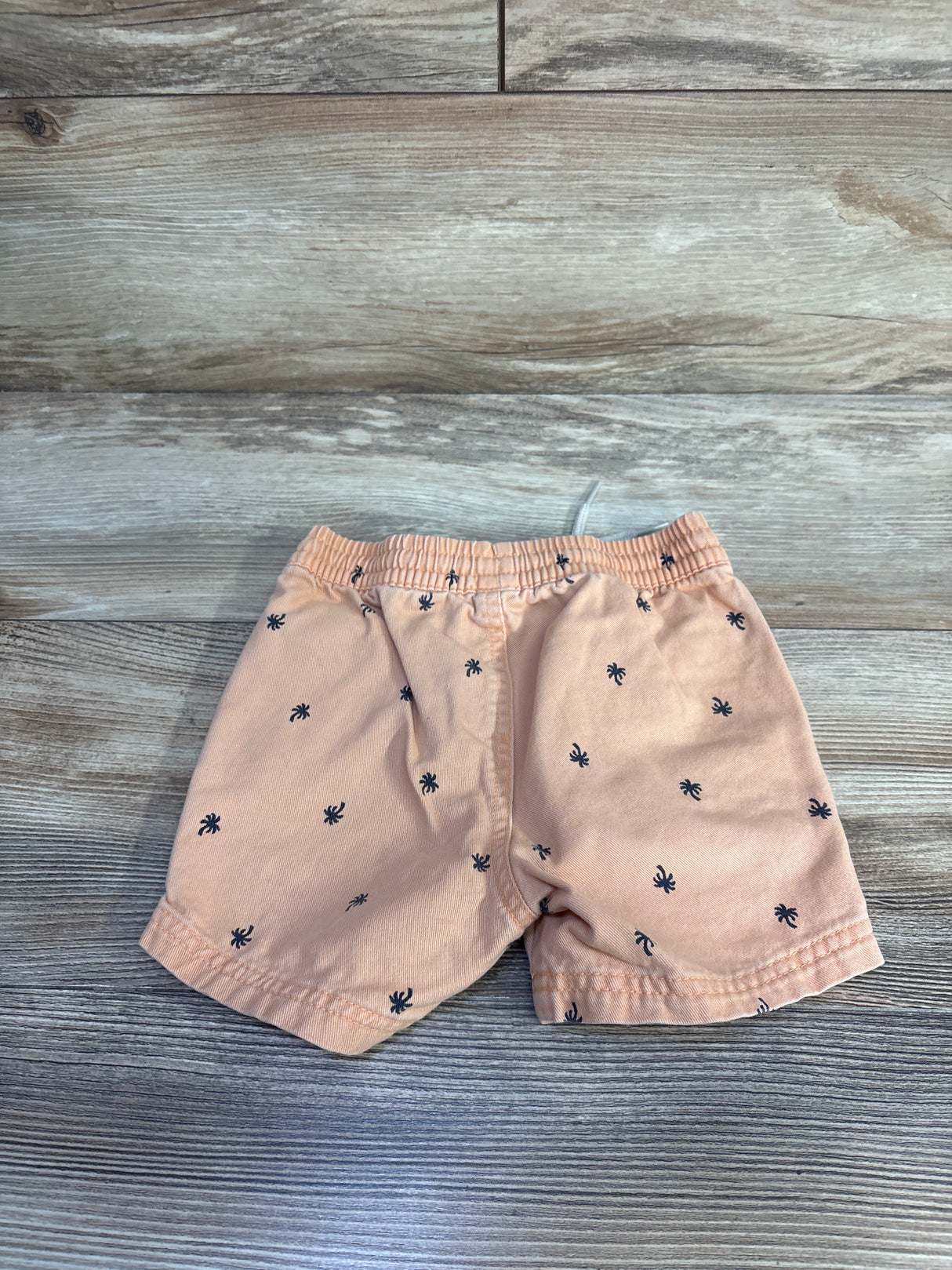Front view of orange toddler twill shorts showcasing elastic waistband and navy palm tree print with wood plank background