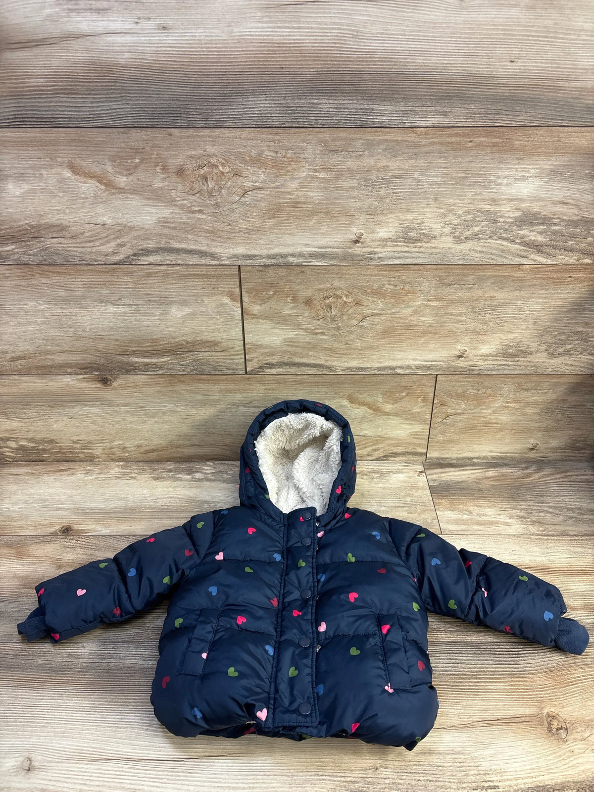 Front flat-lay of Baby Gap navy puffer jacket, 18-24m, with multicolor heart print and sherpa-lined hood on wood background