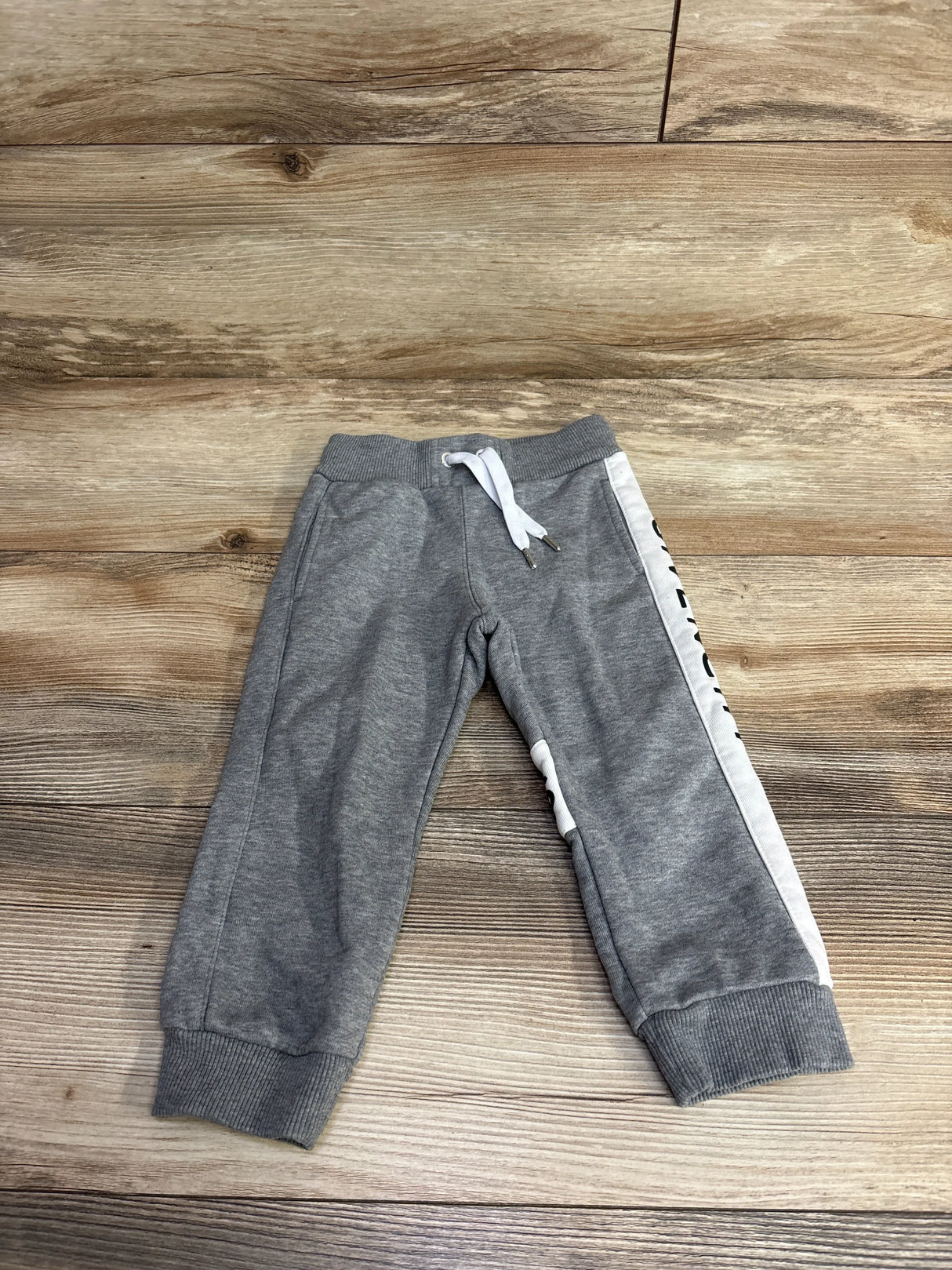 Gray toddler sweatpants with white drawstring and side stripe on wooden floor