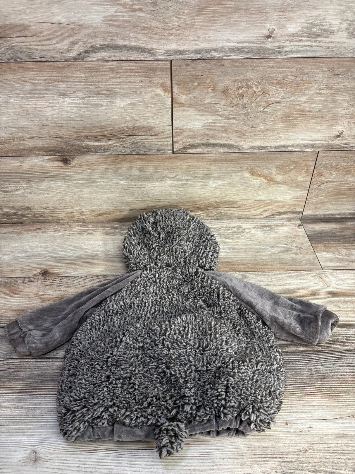 Gray fuzzy baby hoodie with soft texture, laid on wooden floor