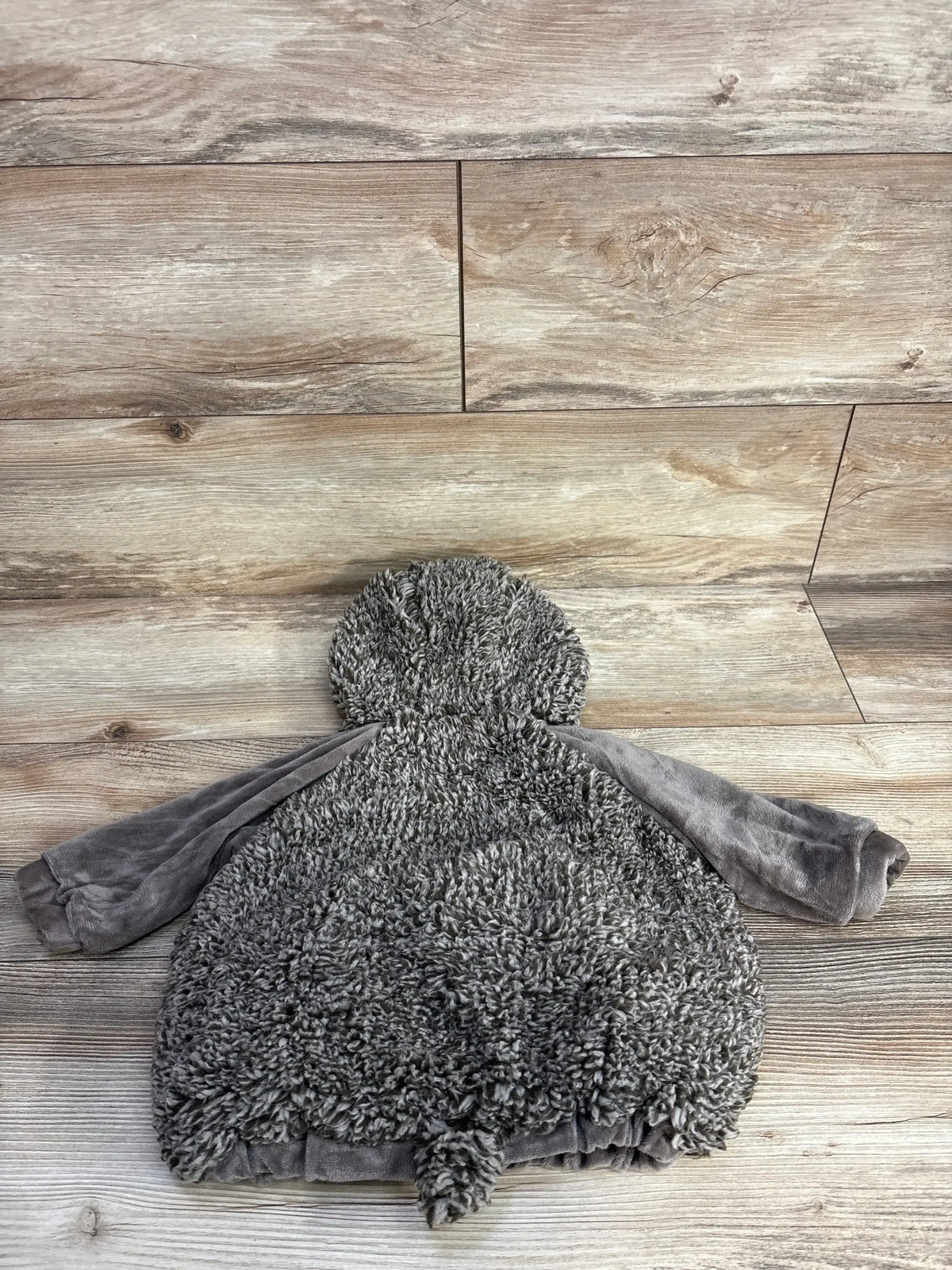 Gray fuzzy baby hoodie with soft texture, laid on wooden floor