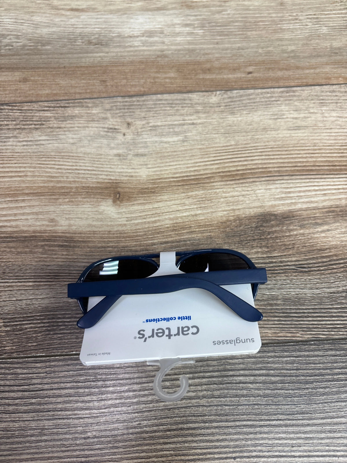 Front view of Carter’s baby sunglasses showcasing dark blue frames and lenses on a product tag against a wood-grain background