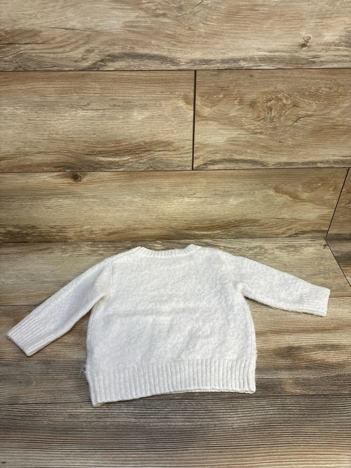 White knit toddler sweater with long sleeves on wood background, gently used kids clothing