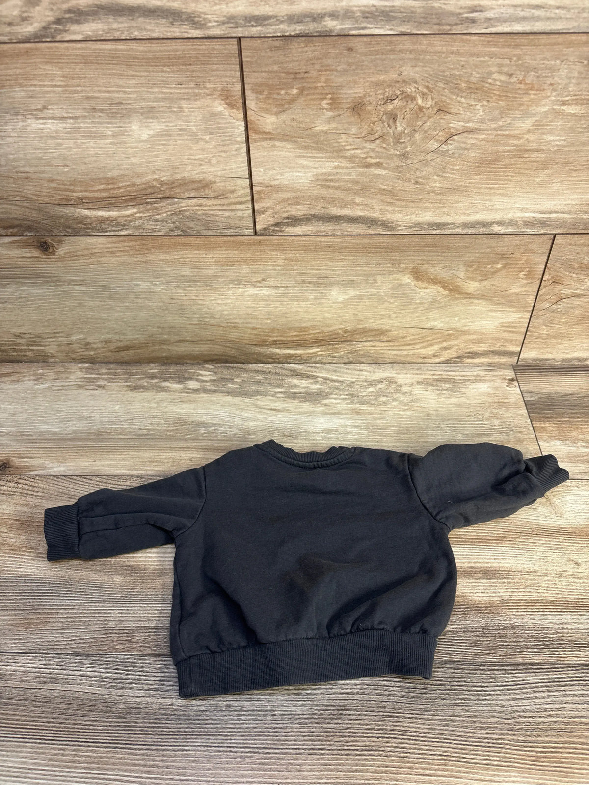 Front view of H&M baby sweatshirt in grey showcasing ribbed crew neck, cuffs, and waistband on a wood-look floor