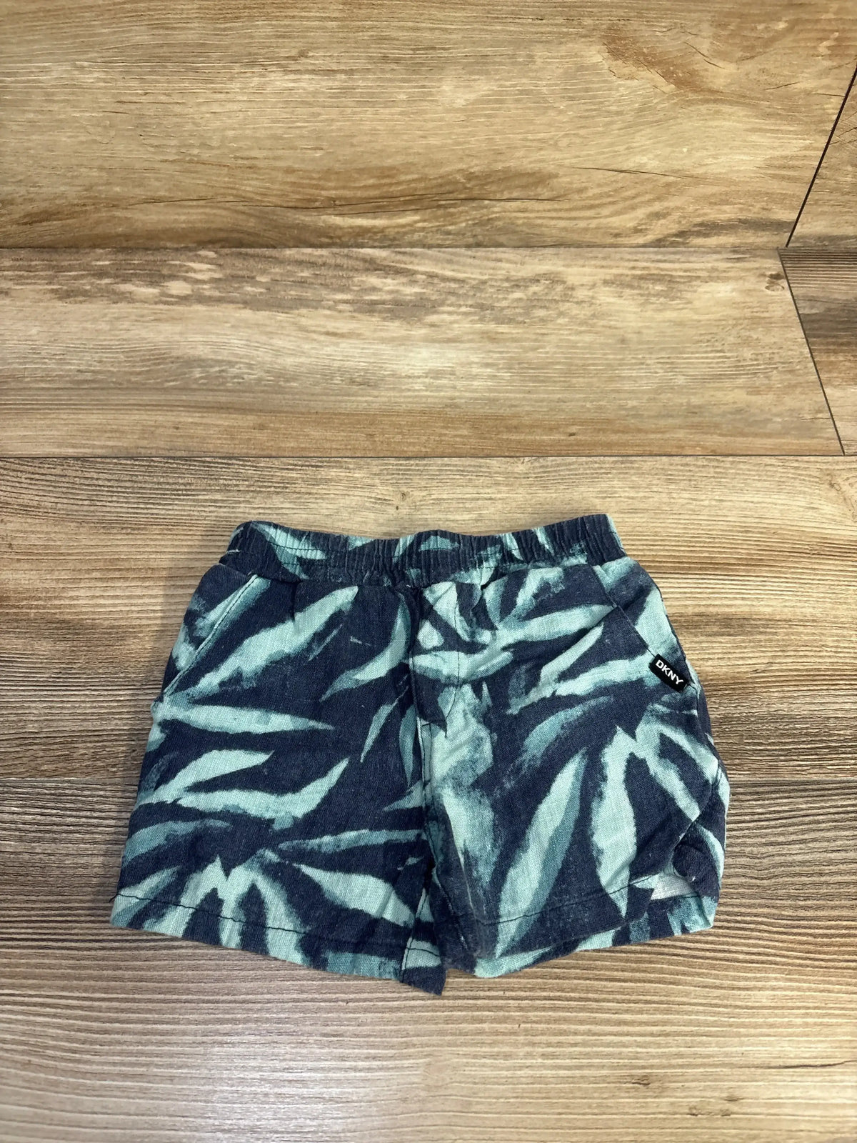 Flat lay of DKNY pull-on linen-blend toddler shorts size 12 months showcasing blue tie-dye print, elastic waistband and side pockets on wood floor