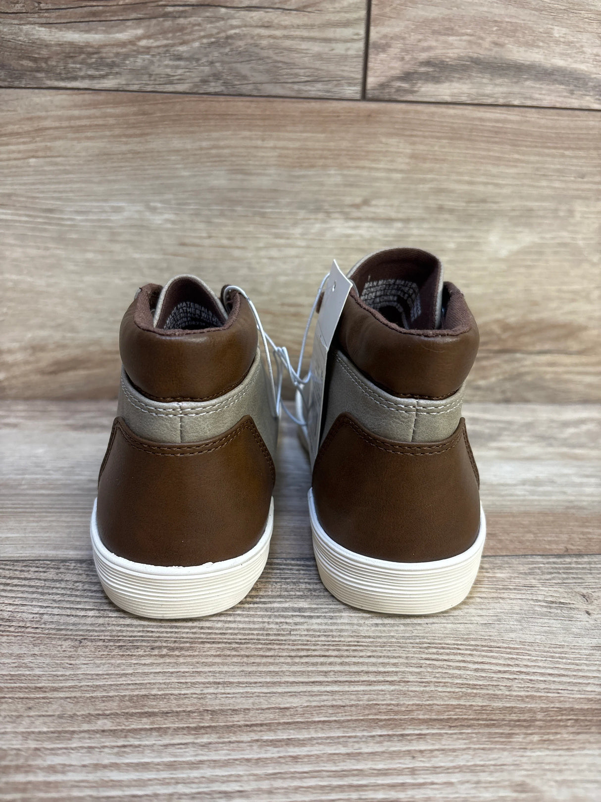Brown and gray toddler high-top sneakers with white soles on wood floor, back view