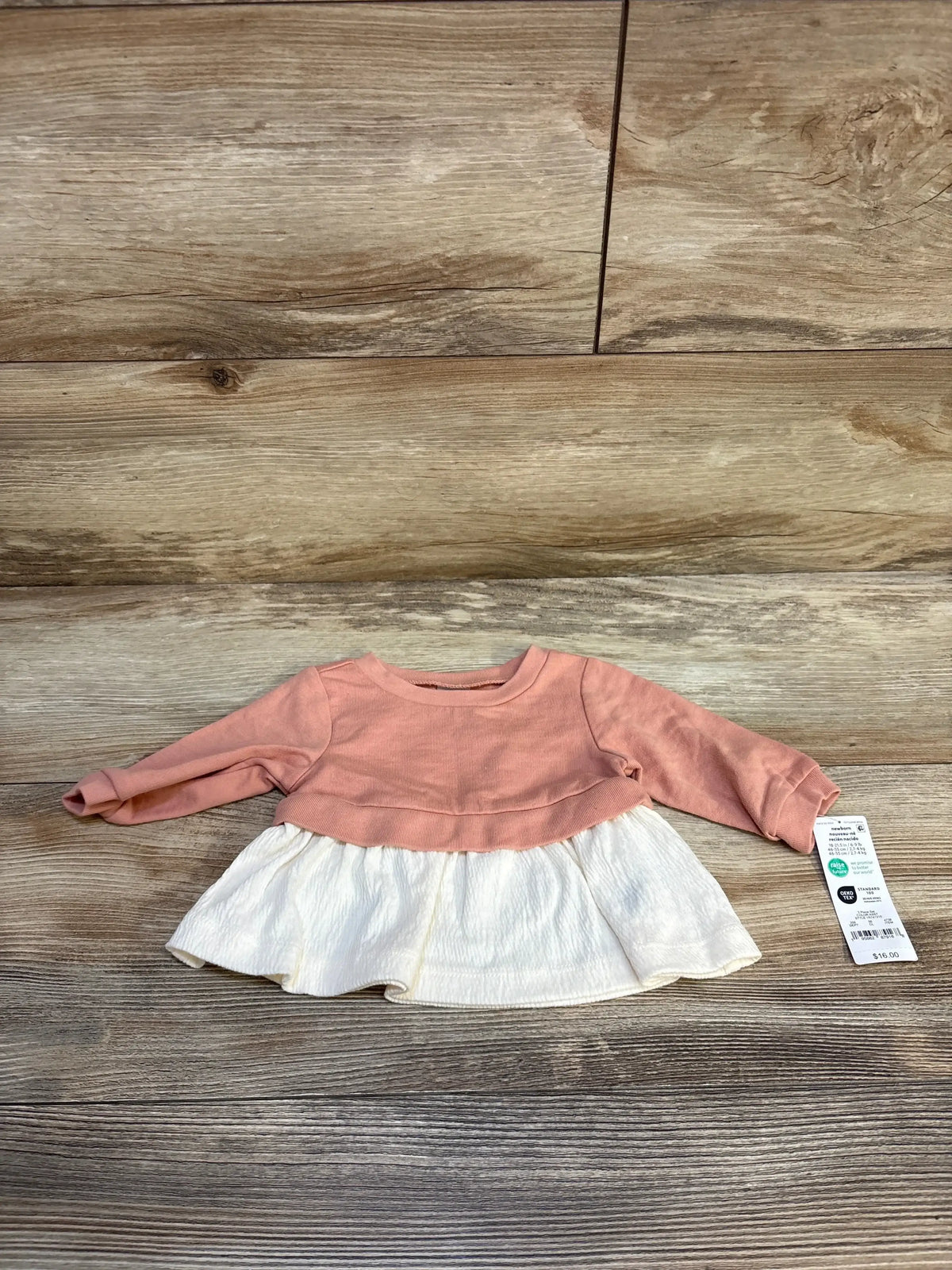 Flat lay of newborn peach peplum sweatshirt showing long sleeves and white textured ruffle skirt on wood floor