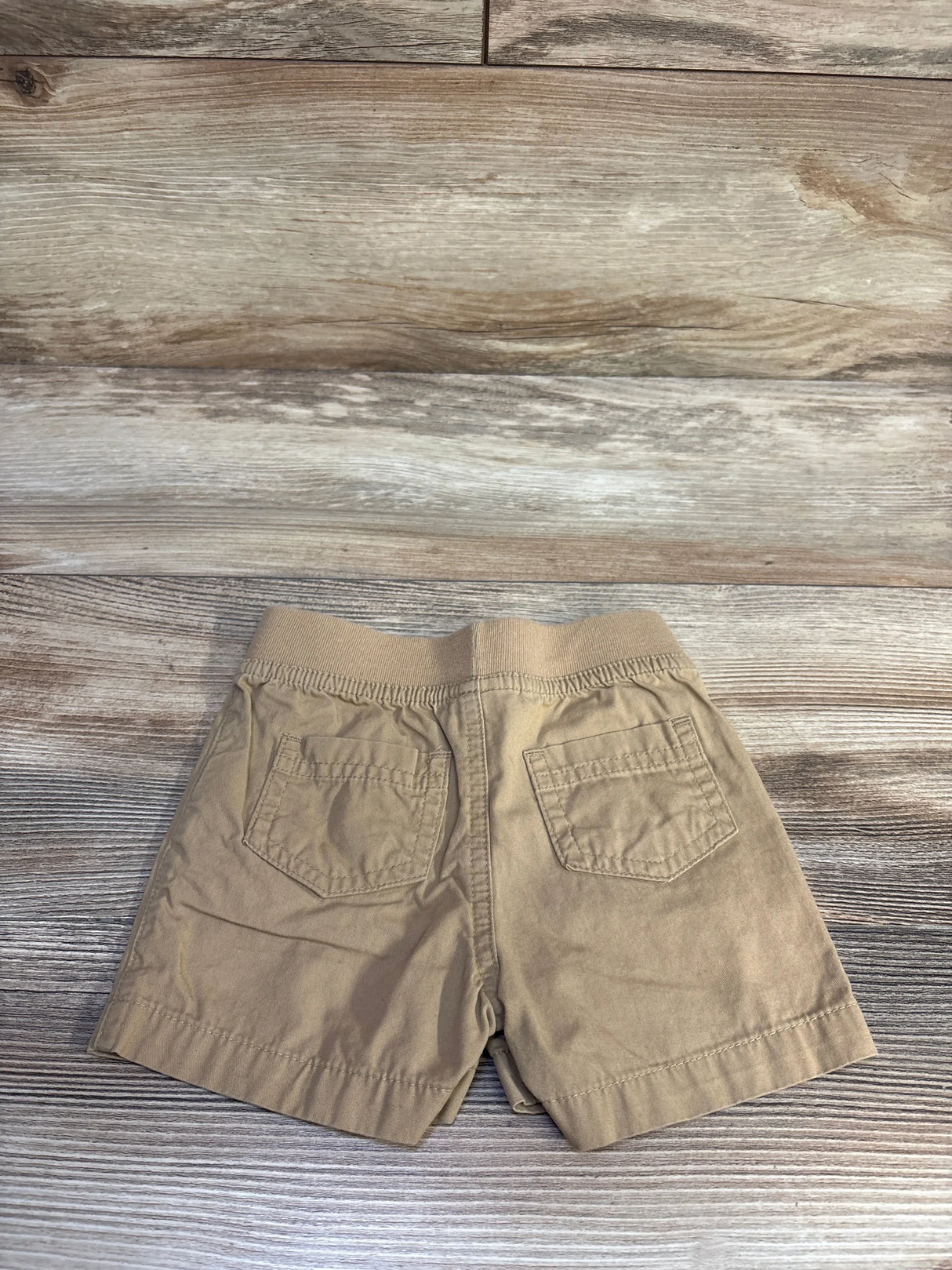 Back of tan Cat and Jack drawstring shorts with elastic waistband and two back pockets on wood background, size 3-6M