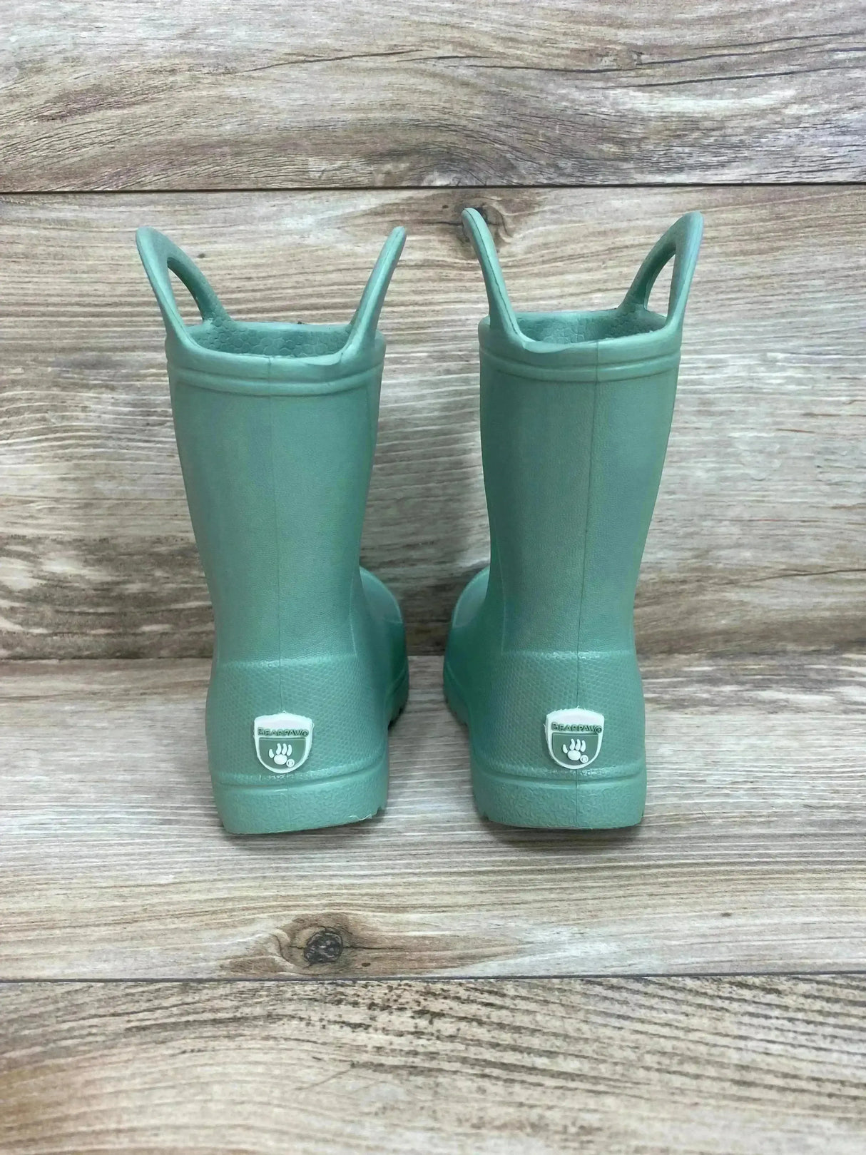 Back view of BEARPAW Toddler EVA Rain Boots sz 3c in mint green with easy pull-on handles and white logo on heel on wood plank floor
