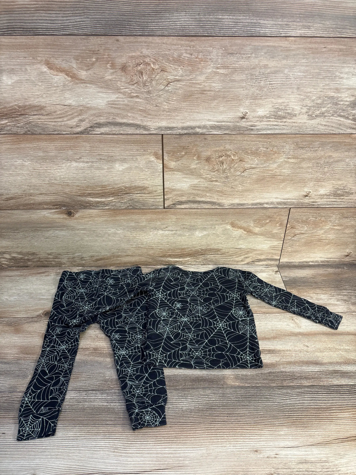 Flat lay of Old Navy two-piece pajama set showcasing black spiderweb print with a wood-look background
