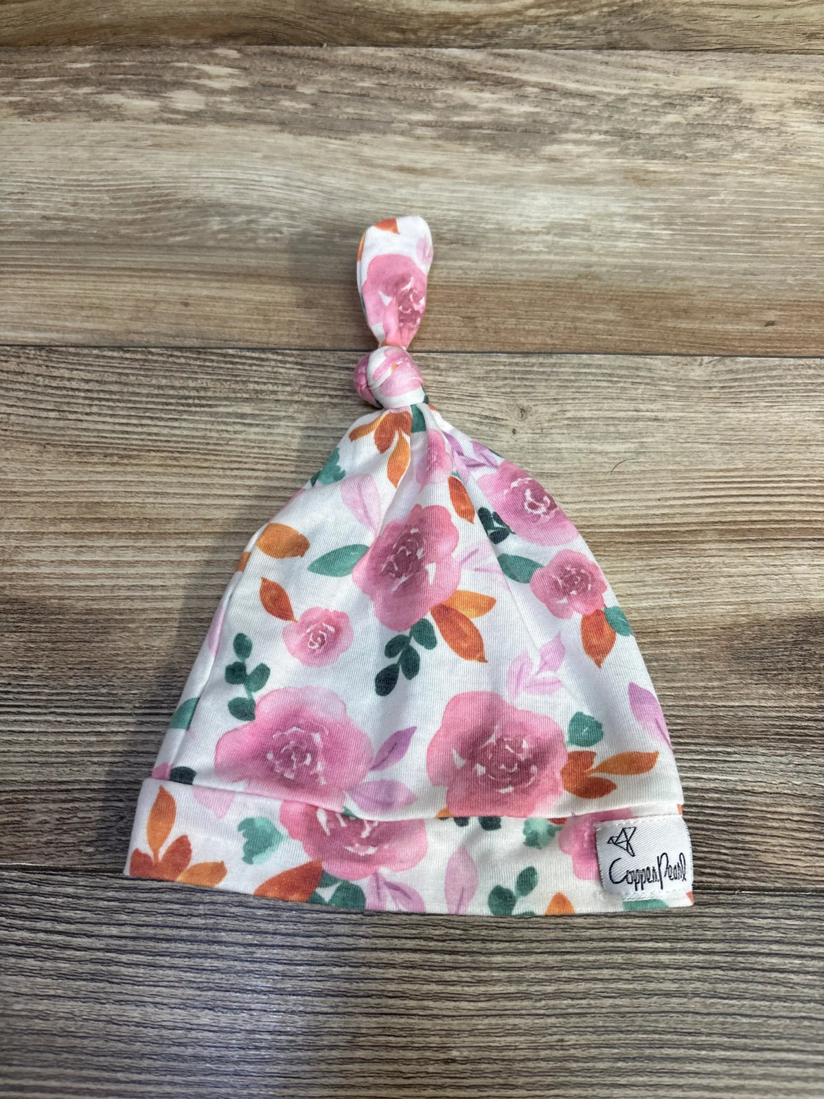Floral baby knotted hat with pink and orange flowers on wood background, Copper Pearl label