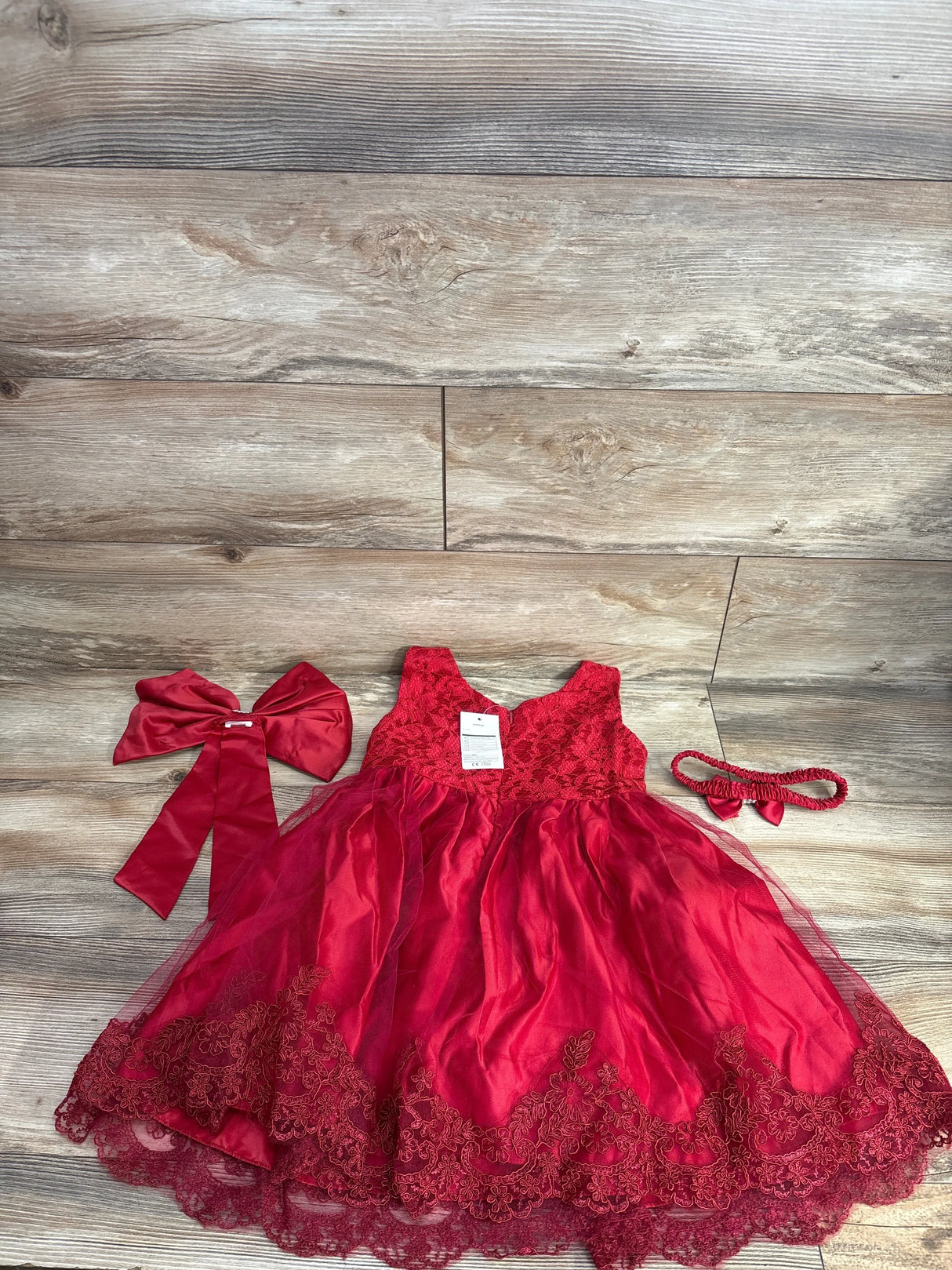 Red lace toddler dress set with matching bow and headband on wood background