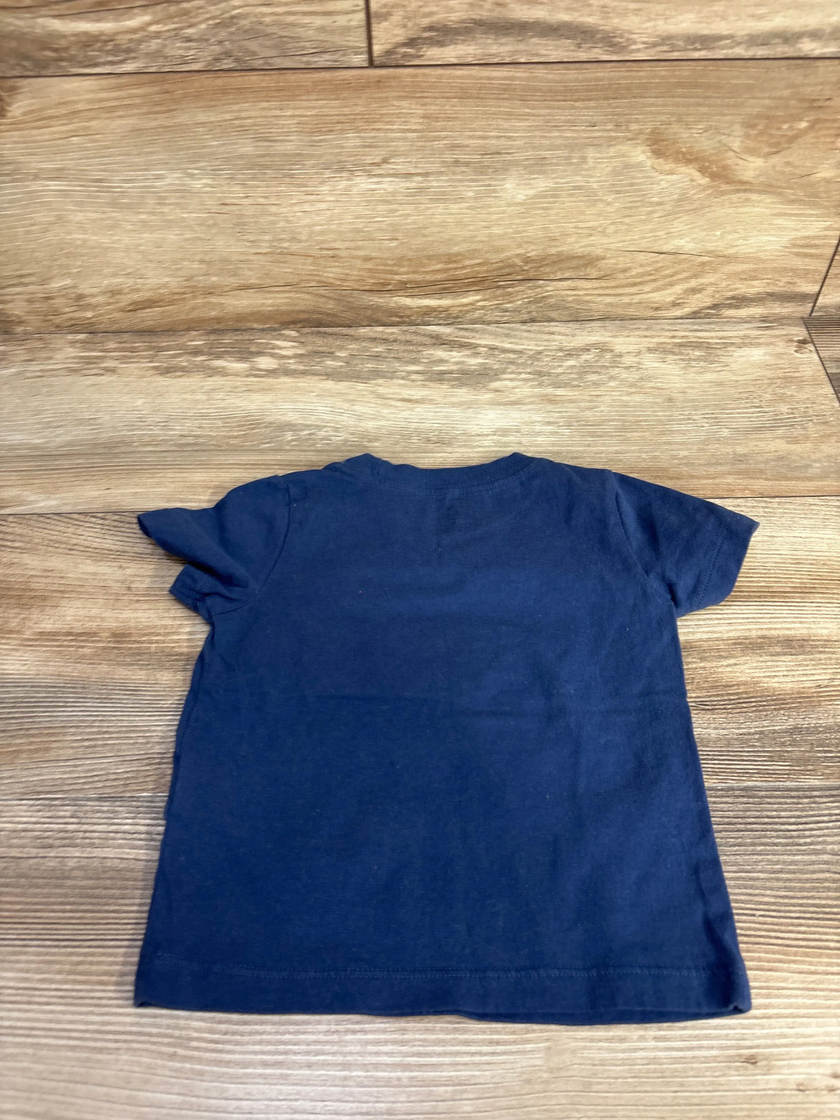 Back view of Carter's navy 18m dinosaur T-shirt showcasing plain back and short sleeves, laid flat on wood floor