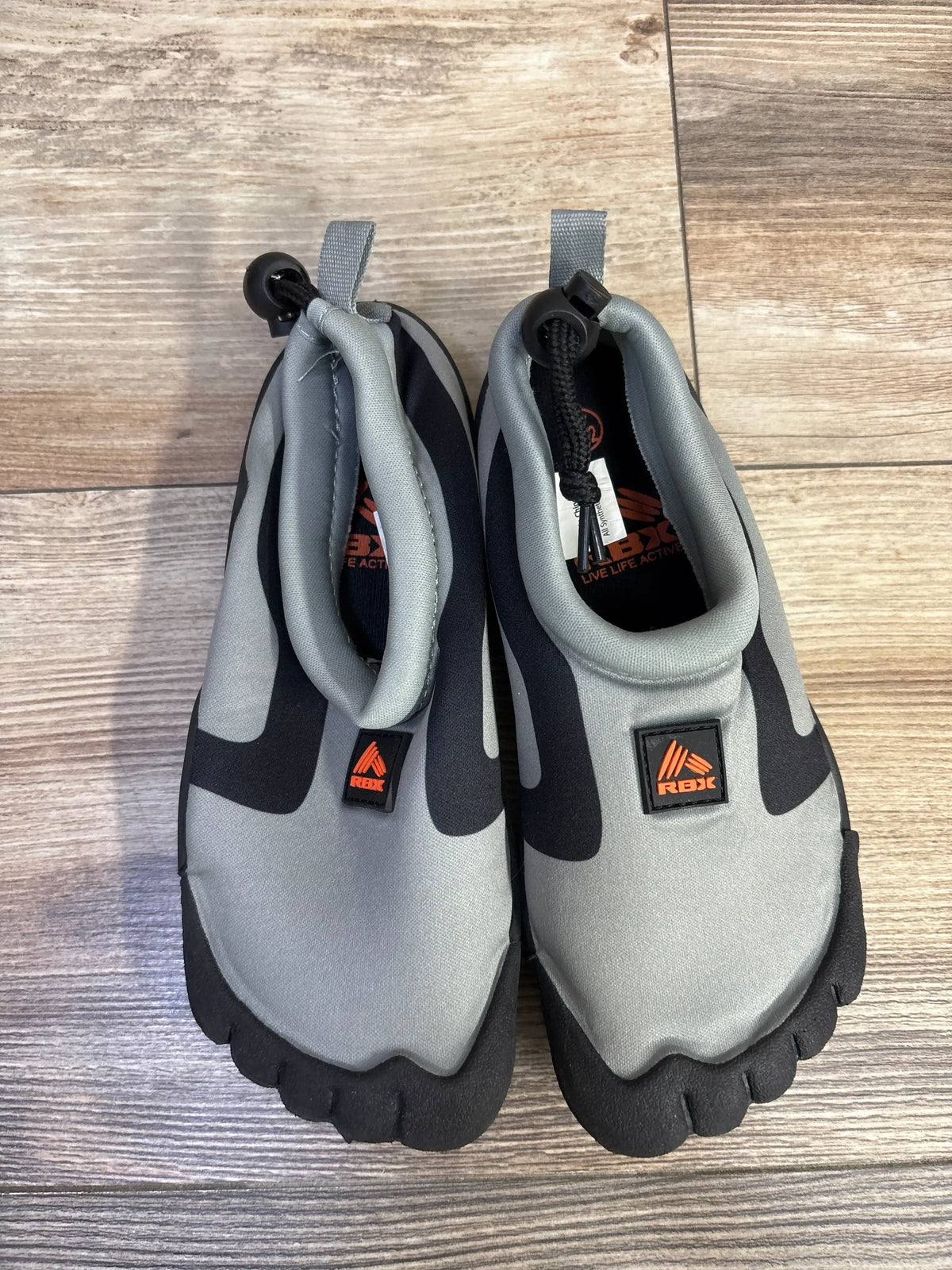 Top-down of RBX grey toddler water shoes size 11/12 with black split-toe soles, orange logo, heel drawstrings on wood floor