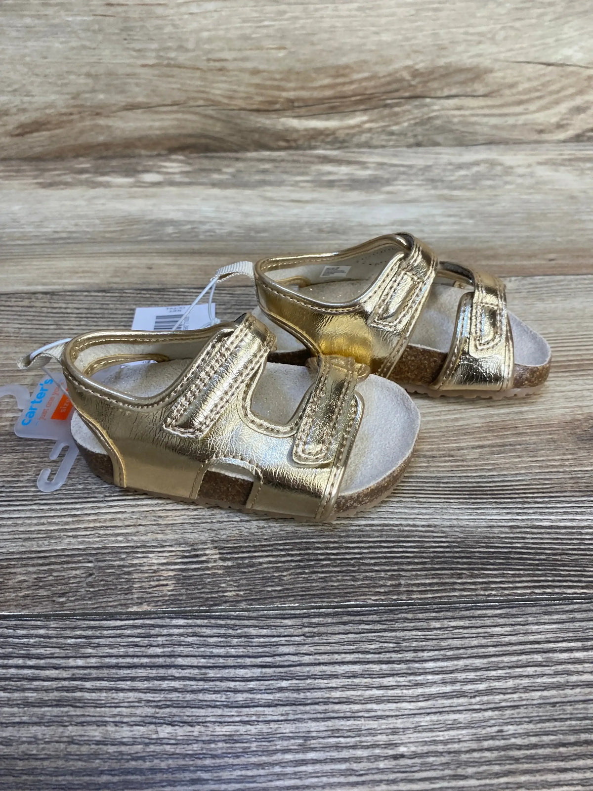Gold toddler sandals with velcro straps and cork soles on wood background